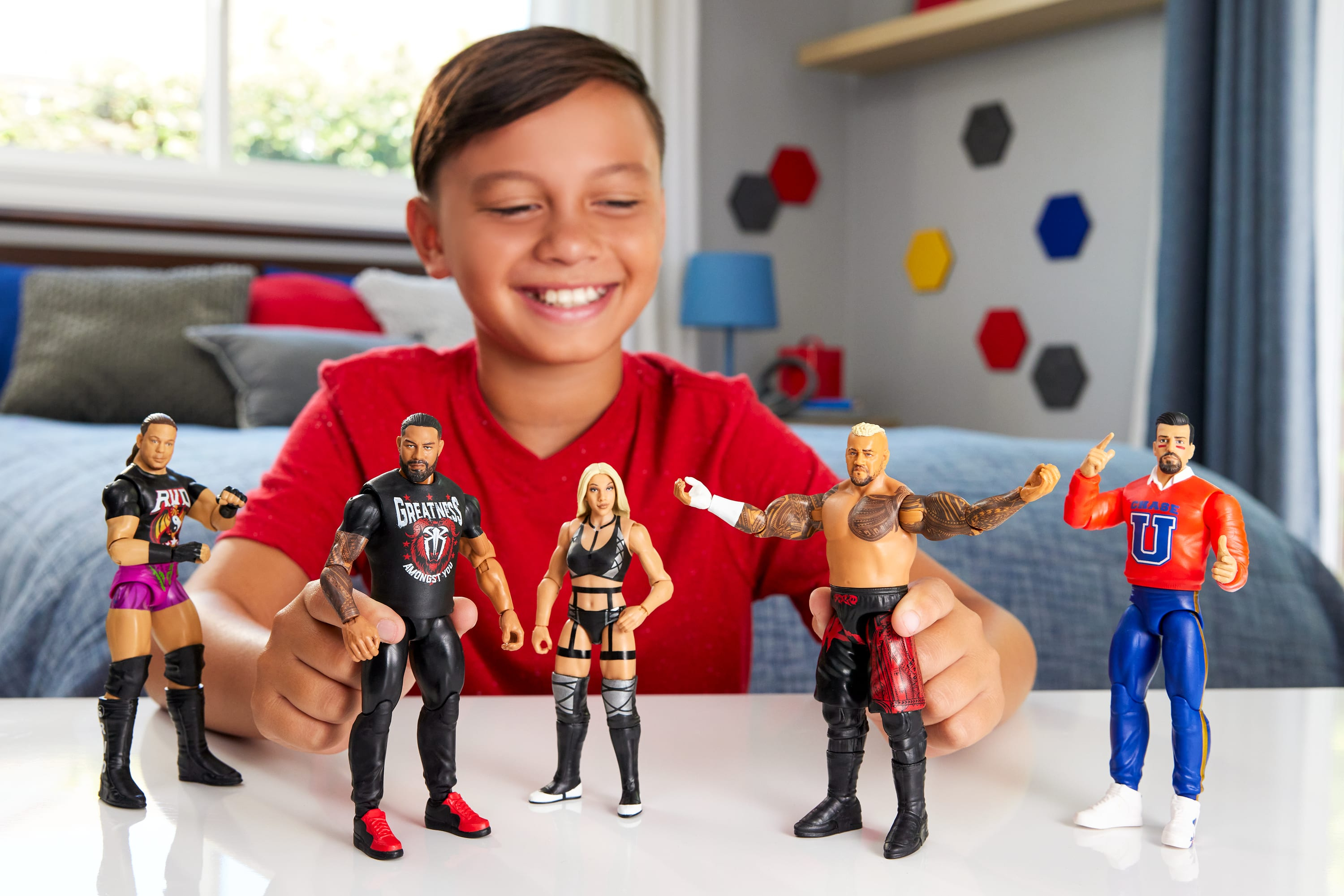 Un ragazzo che gioca con le figure di wrestling. Cinque figure sono disposte su una superficie bianca di fronte al ragazzo.