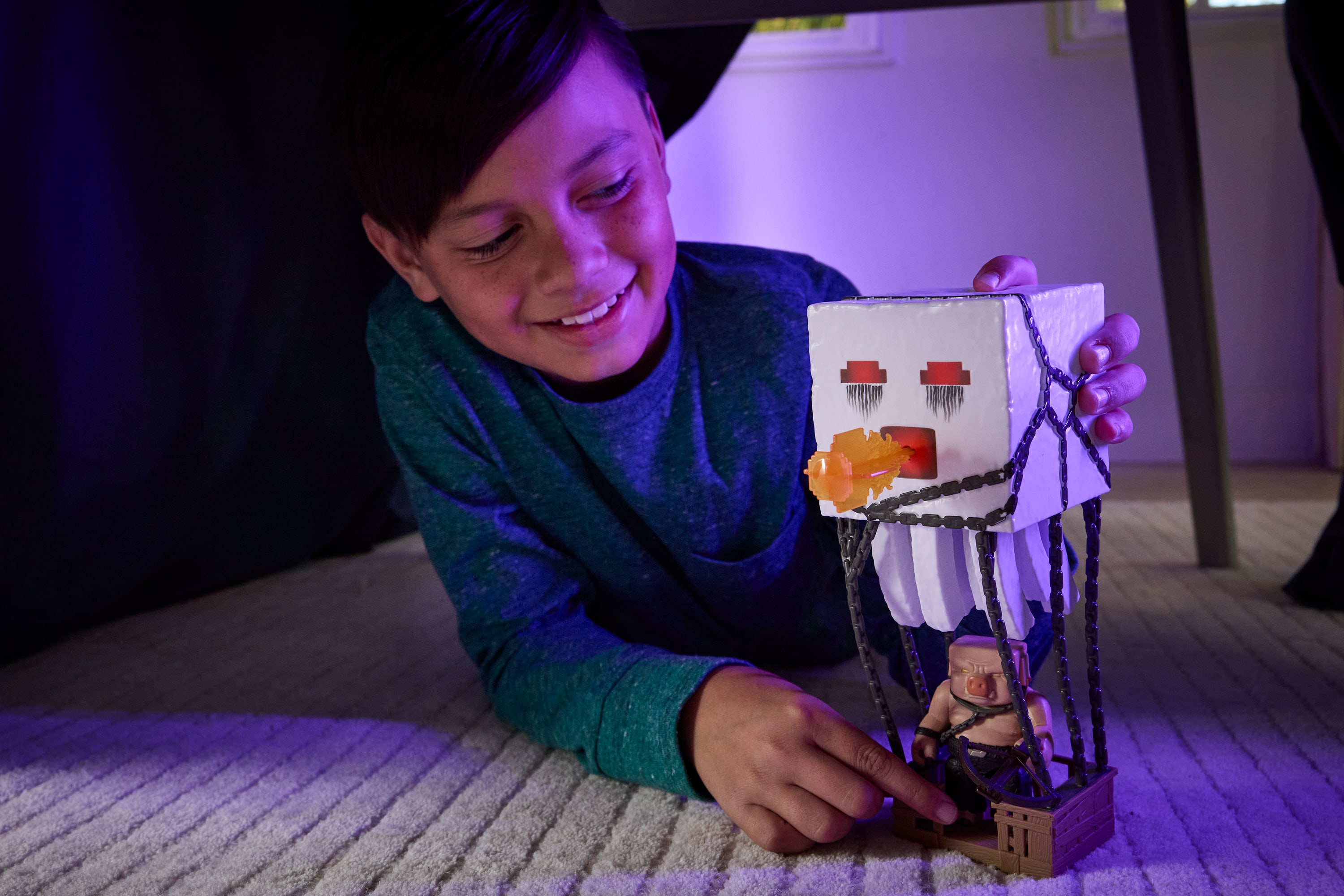 Chłopiec uśmiecha się, bawiąc się zabawką Minecraft. Zabawka to figurka w środowisku Minecraft.