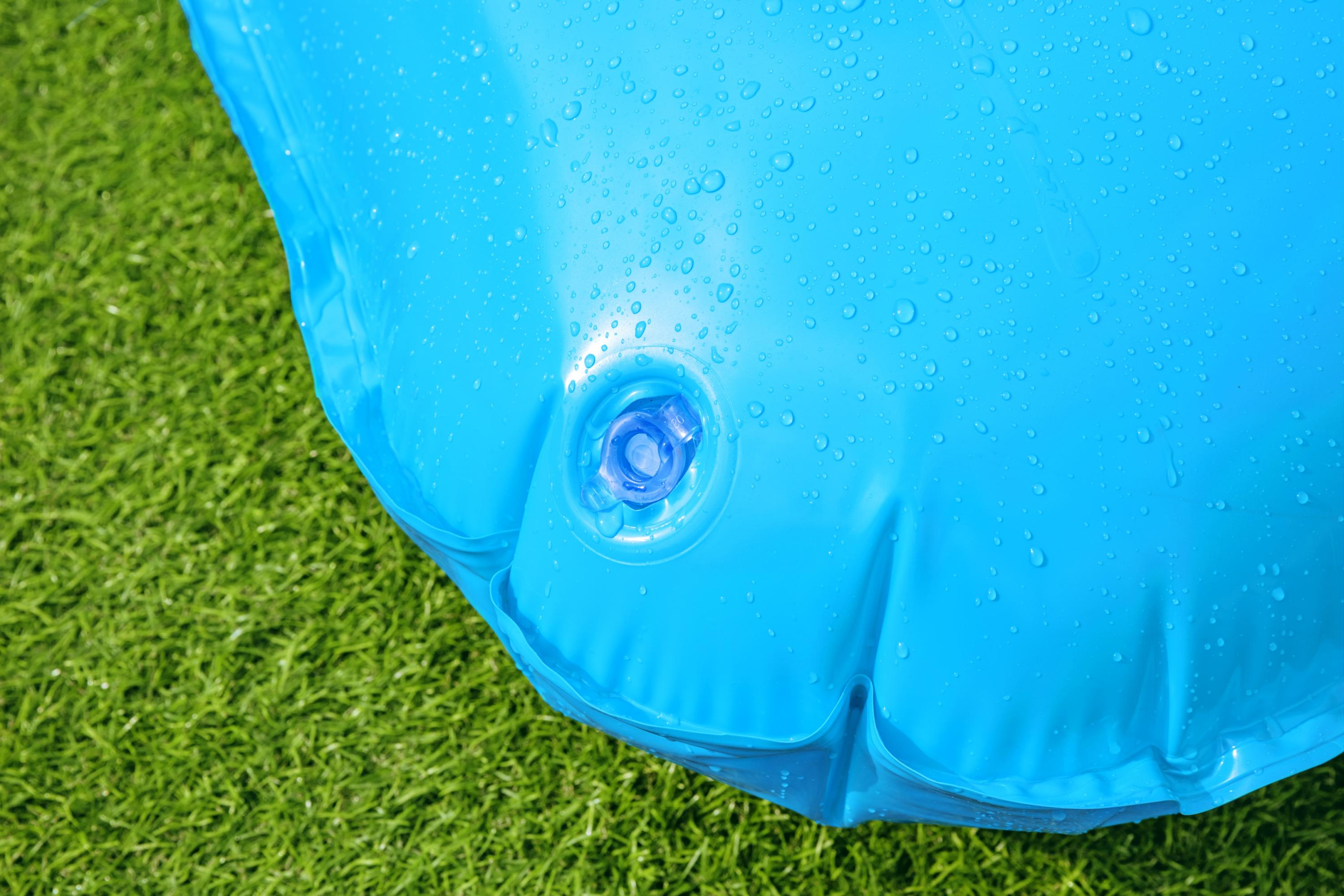 Niebieski basen dmuchany na zielonej trawie. Niebieski zawór jest widoczny na środku basenu. Krople wody.