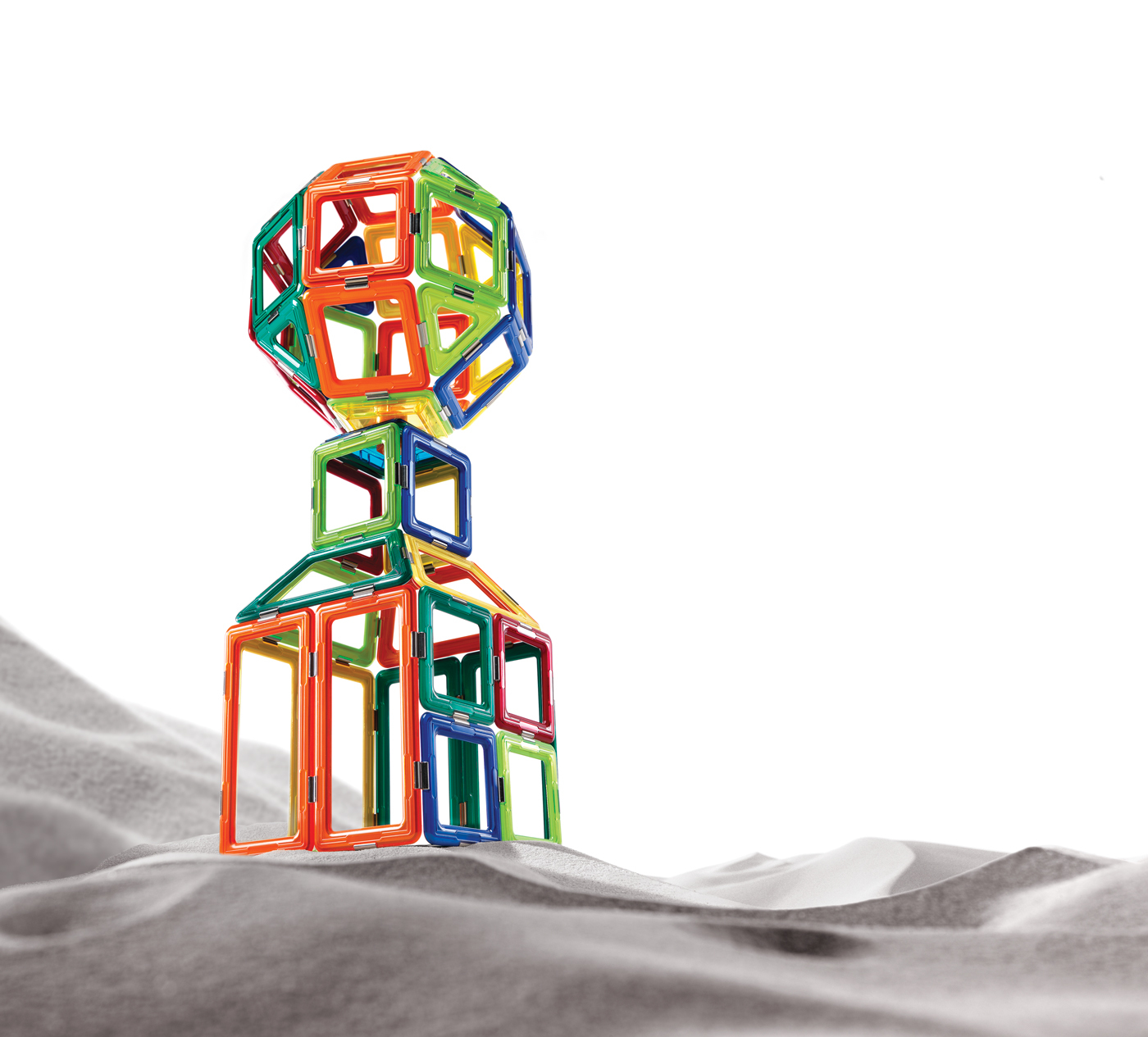 Una struttura geometrica multicolore composta da forme interconnesse, su uno sfondo di sabbia in scala di grigi.