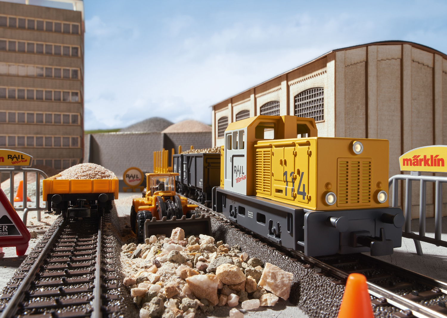 Scena del trenino con una locomotiva diesel gialla, vagoni e oggetti di cantiere.