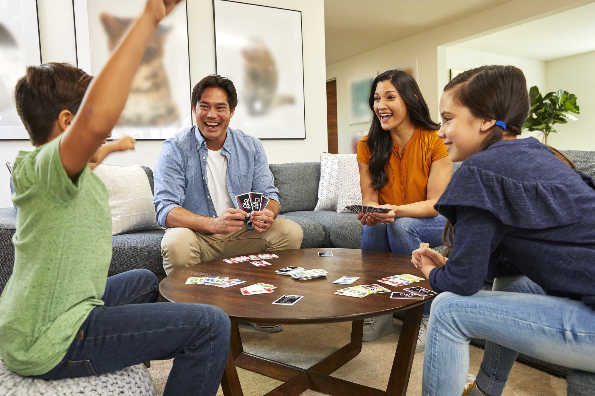 Famille jouant aux cartes sur une table basse. Un garçon lève les bras. D'autres rient.