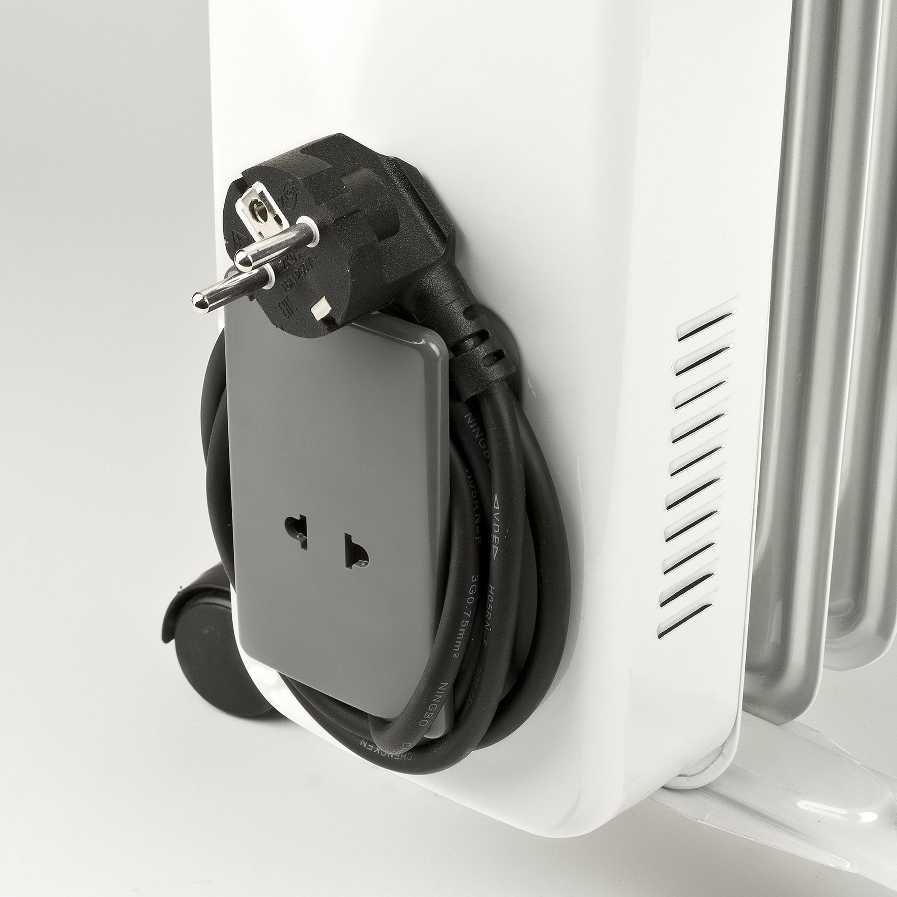 Biały grzejnik z kablem zasilającym i szarym gniazdkiem. Białe tło.