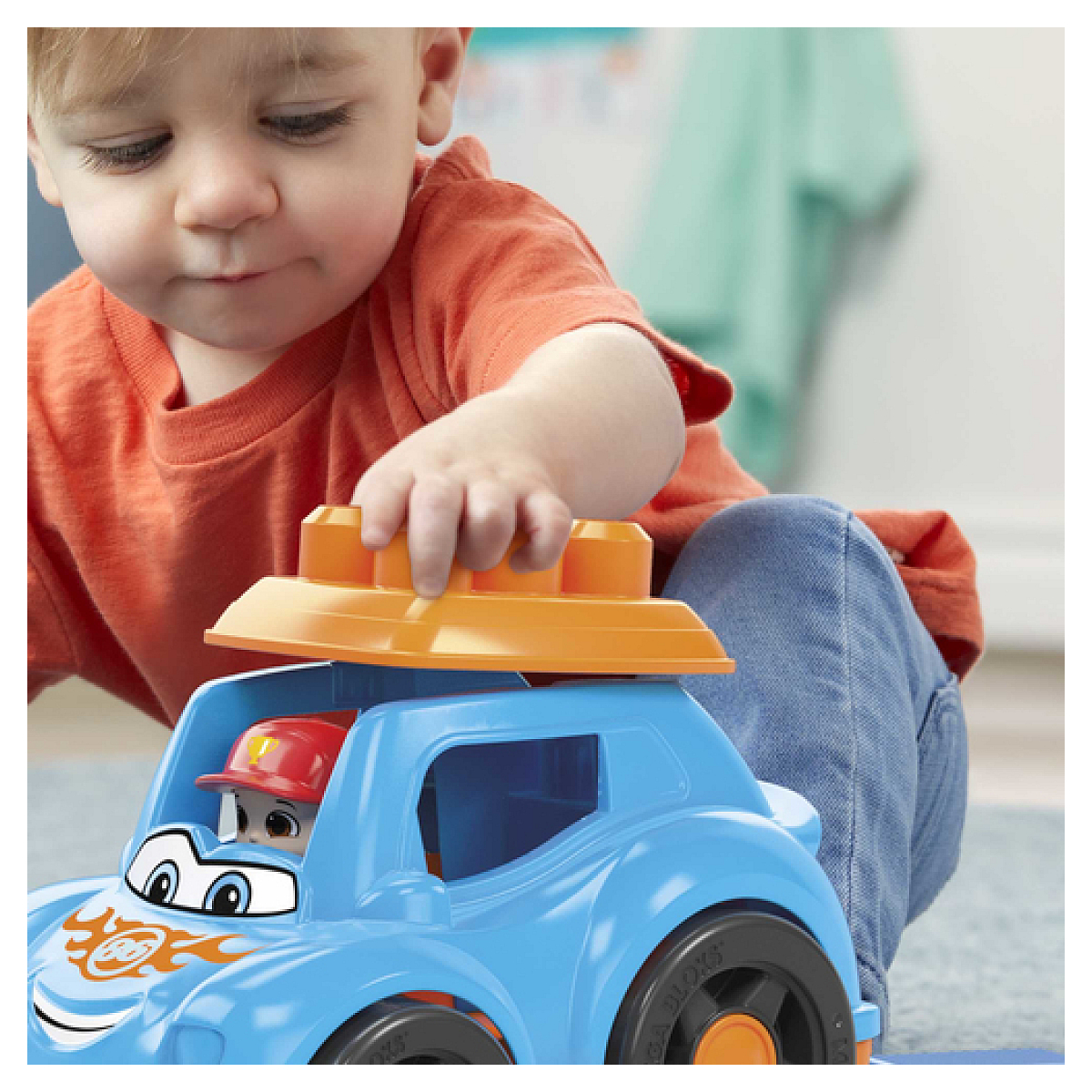 Un niño juega con un coche de juguete azul y naranja. Un conductor de juguete en el coche, sobre fondo blanco.