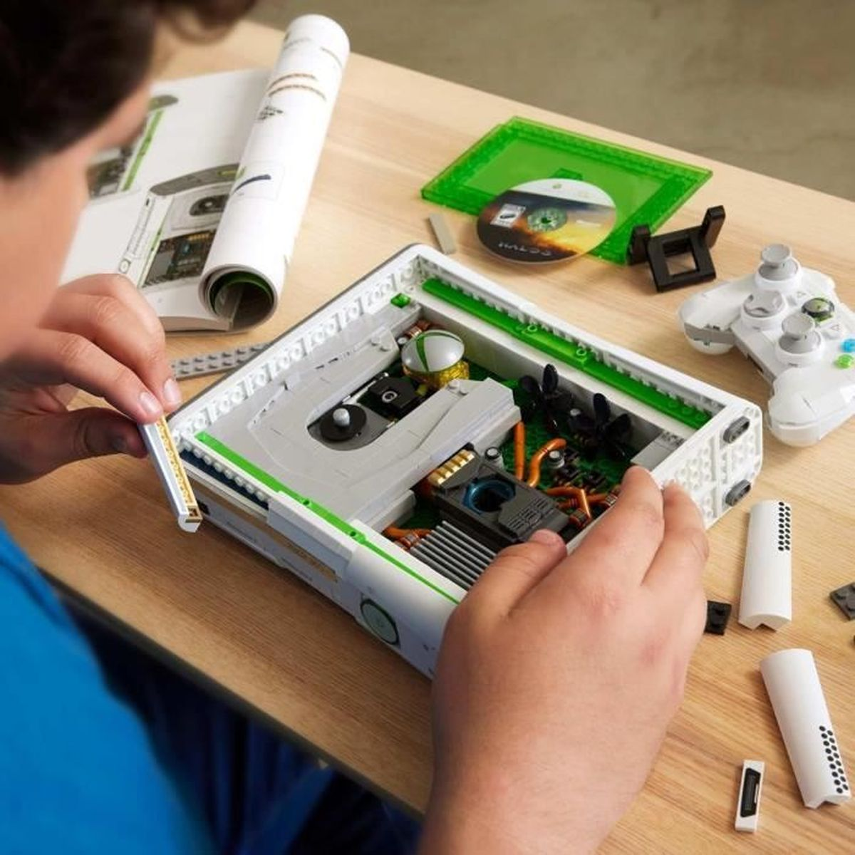 Osoba składająca model Lego Xbox. Konsola jest biało-zielona z otwartą tacką.