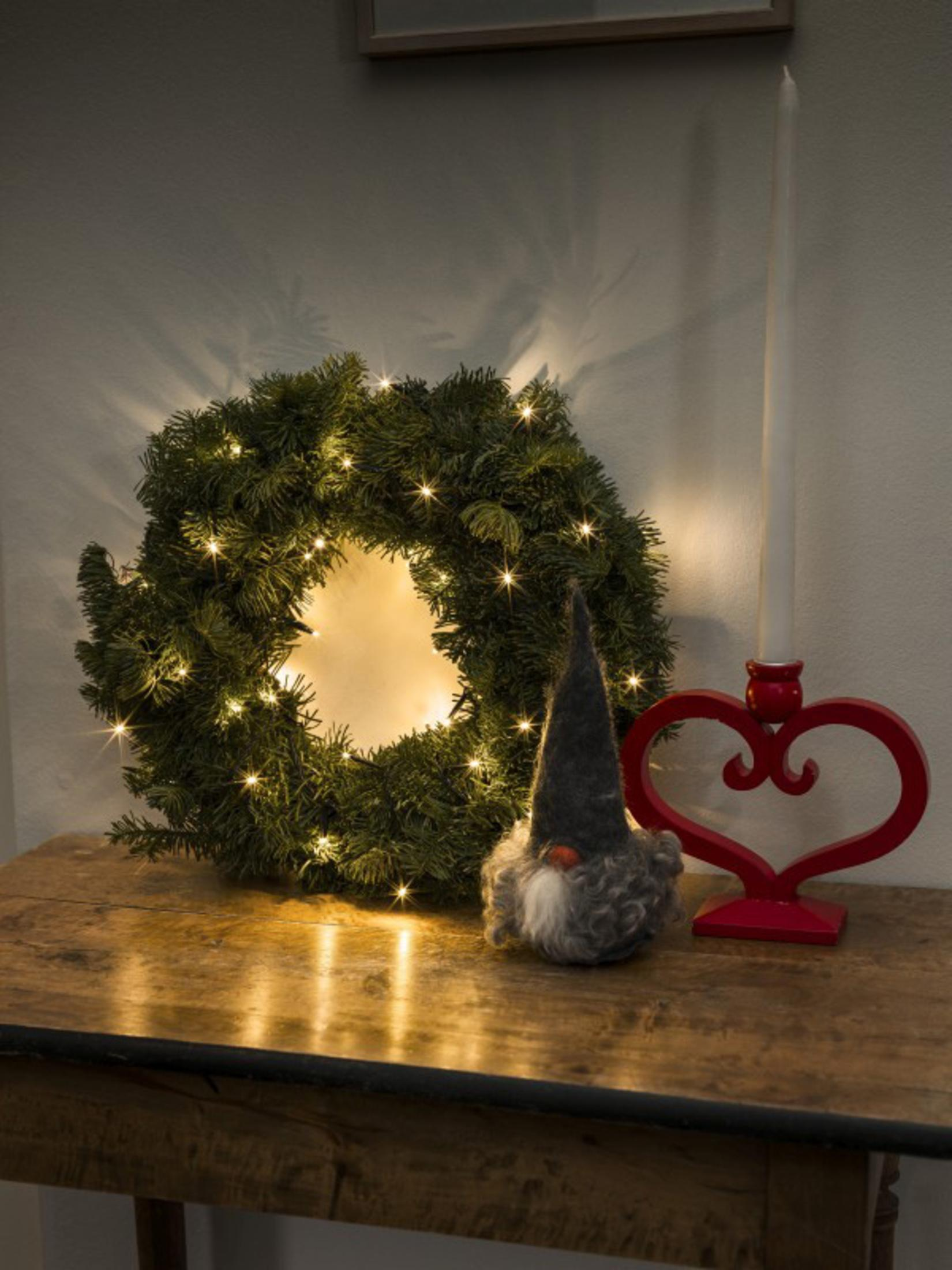 Eine Weihnachtsdekoration auf einem Tisch mit einem Kranz, Lichtern, einem Wichtel und einem Kerzenhalter.