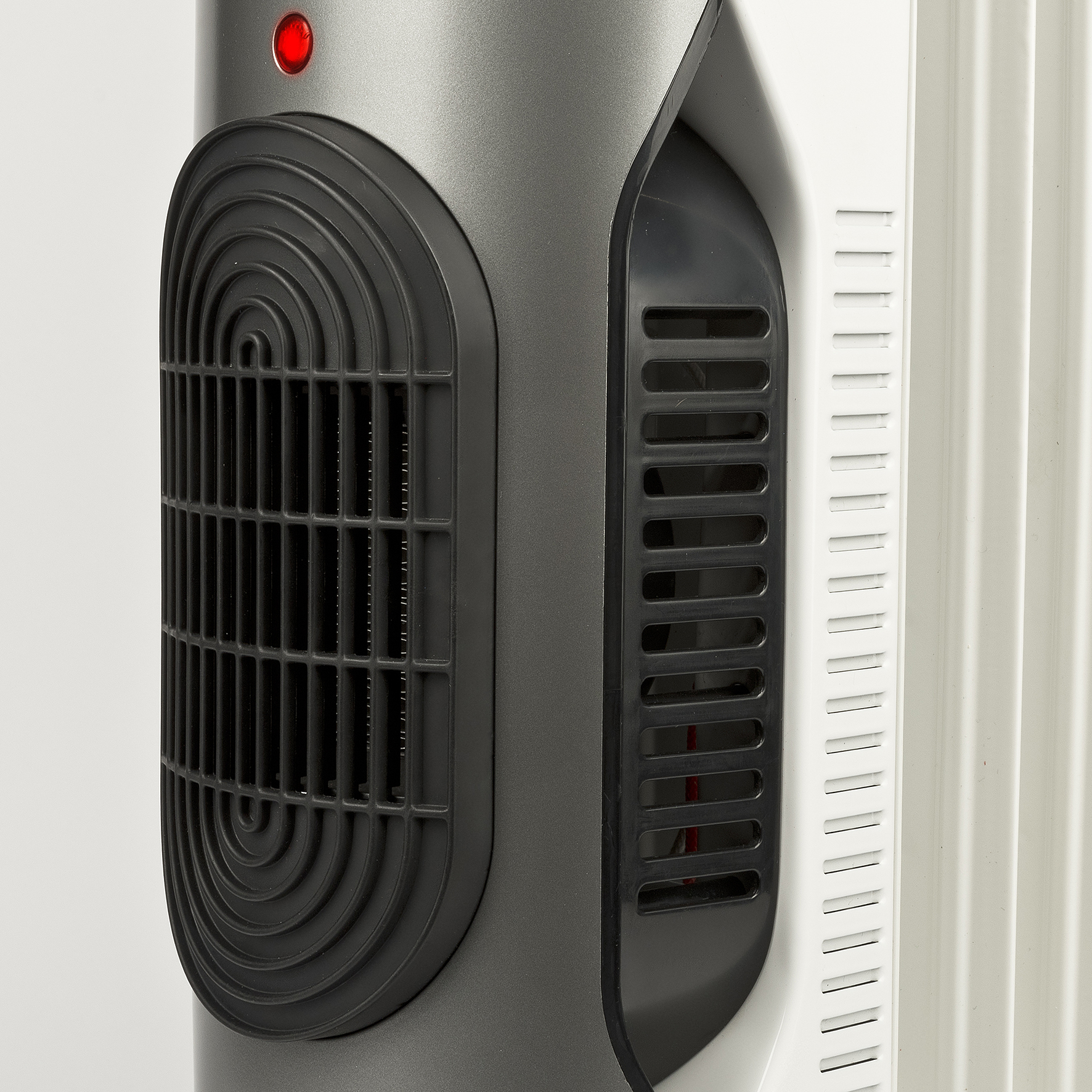 Zbliżenie grzejnika elektrycznego z czerwonym światłem i czarną kratką. Widoczne są niektóre żebra.