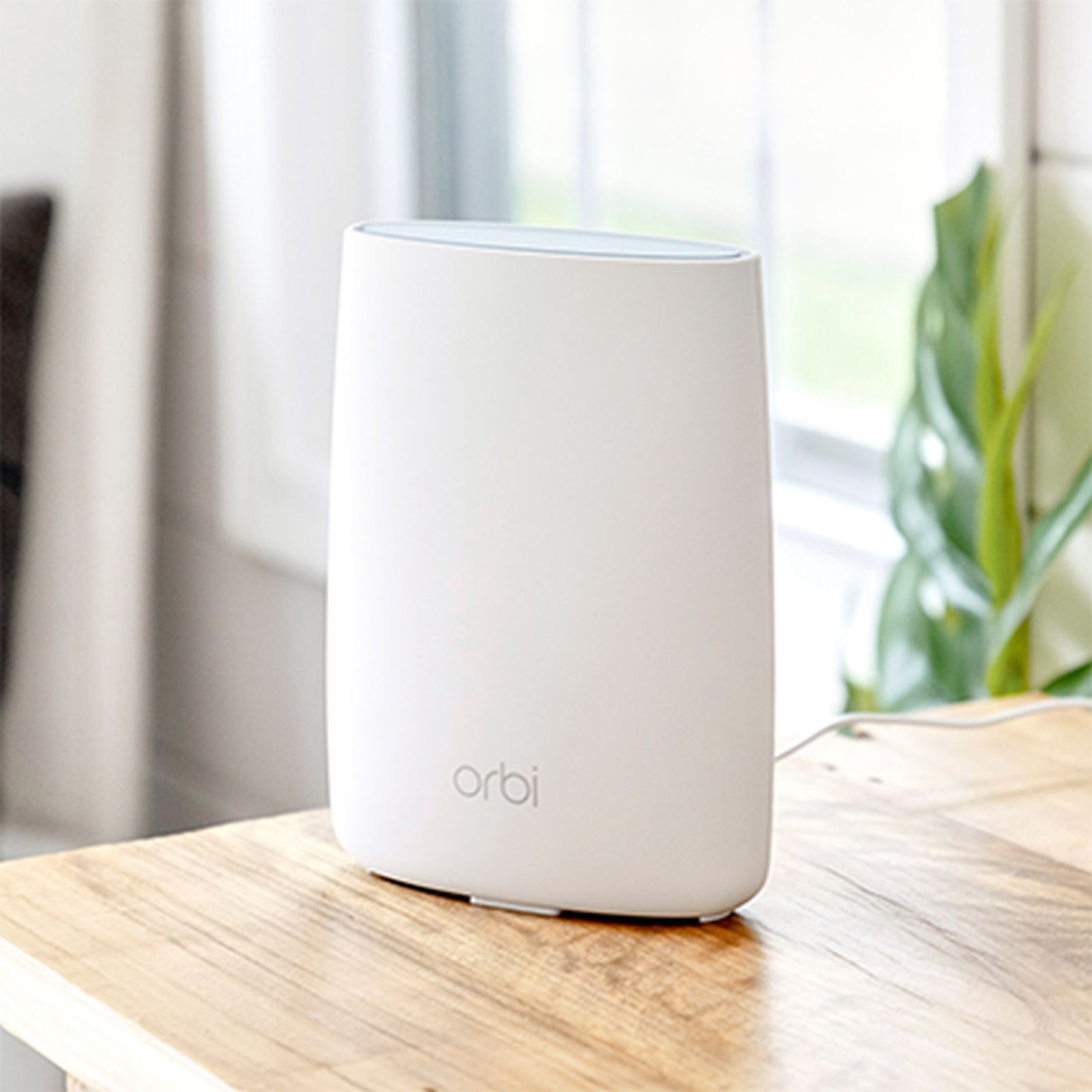 Router Orbi bianco su un tavolo di legno. Una pianta è visibile sullo sfondo.