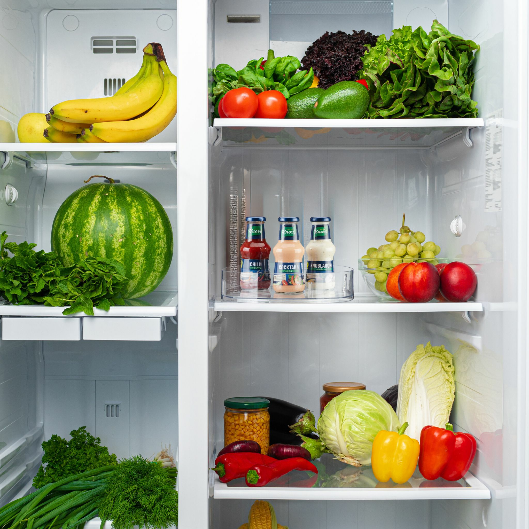 Intérieur du réfrigérateur avec fruits, légumes et condiments sur des étagères. Comprend bananes, pastèque, laitue, etc.