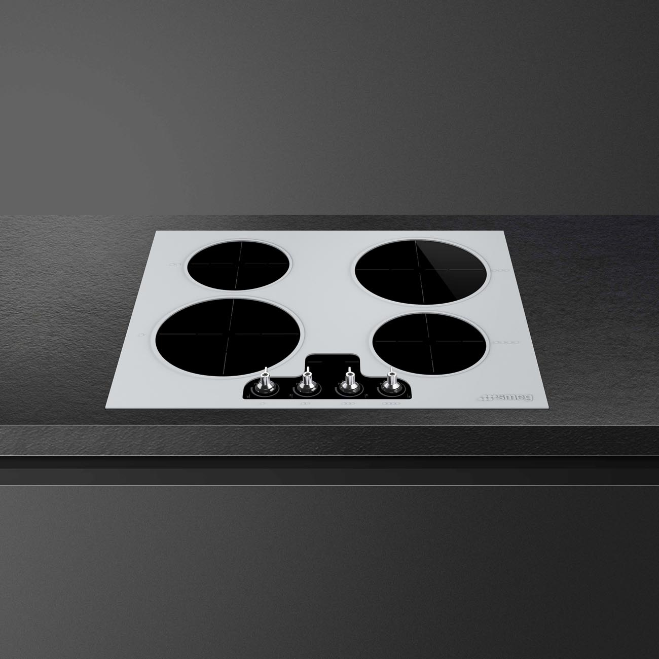 Una placa de cocina blanca con cuatro zonas de cocción negras y cuatro mandos, sobre una superficie negra.