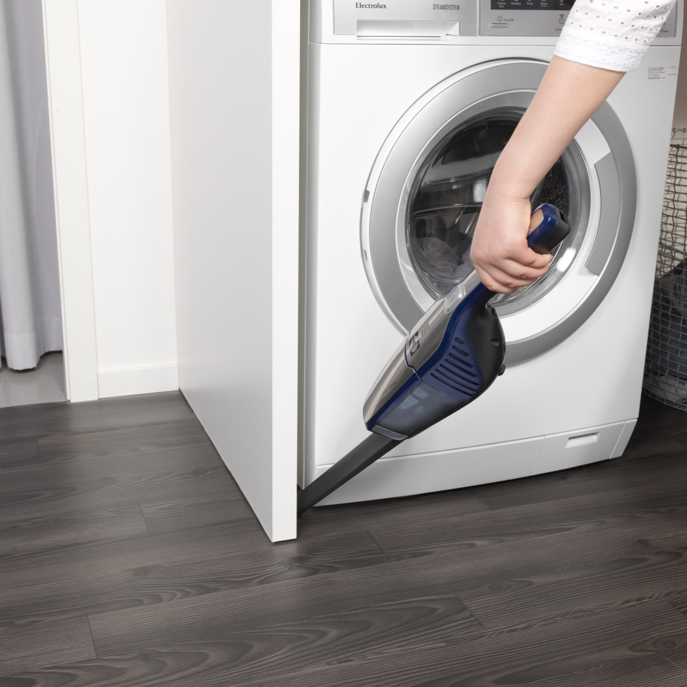 Une femme utilise un aspirateur à main pour nettoyer le long d'un plancher en bois foncé.