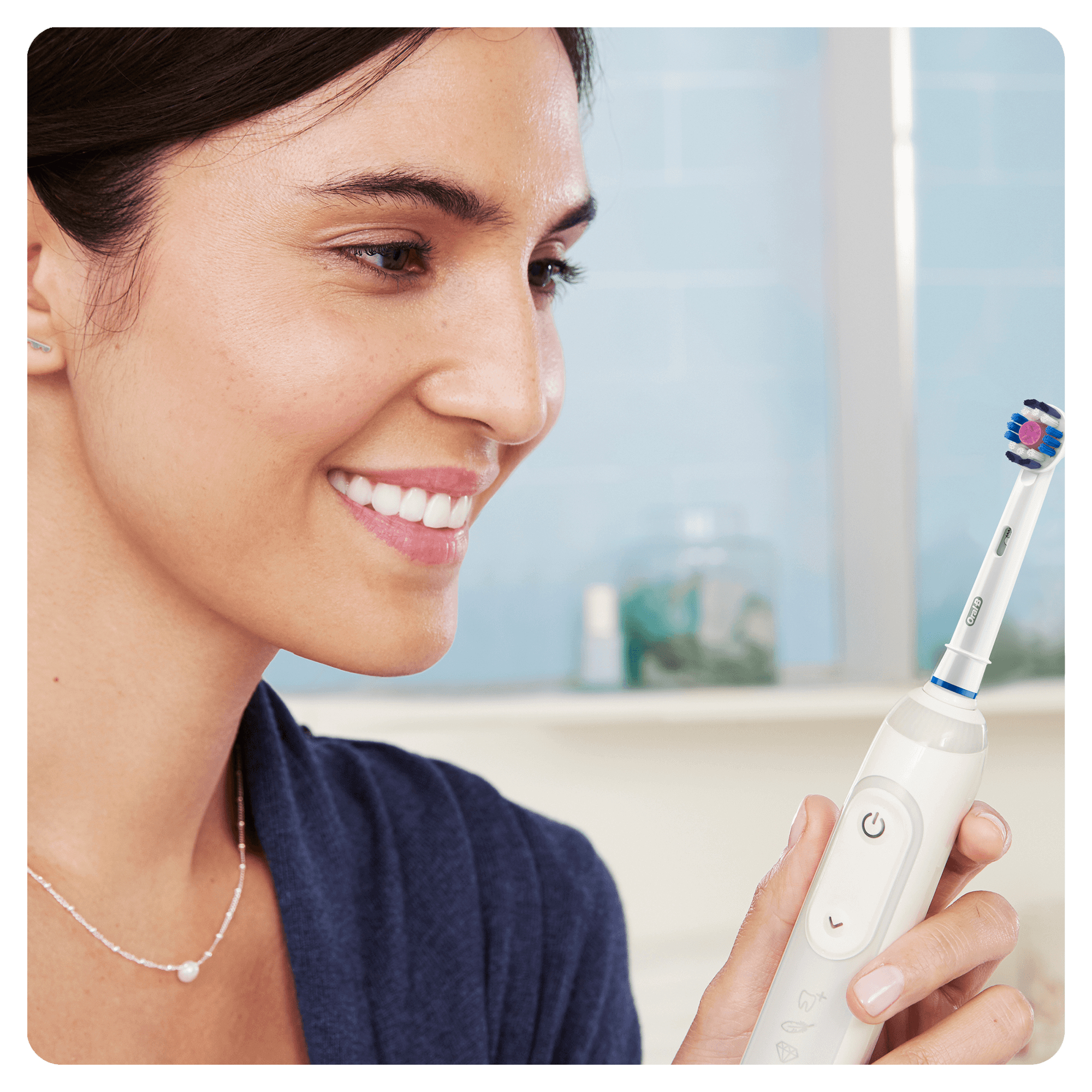 Donna sorridente, tiene uno spazzolino elettrico. Lo sfondo è un bagno. Guarda lo spazzolino.
