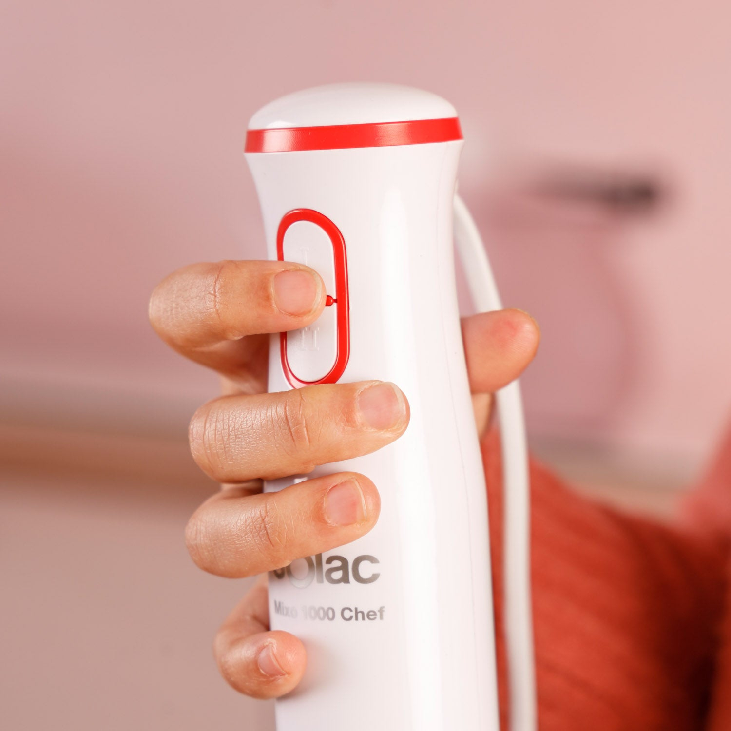 Dłoń trzyma biało-czerwony blender ręczny.