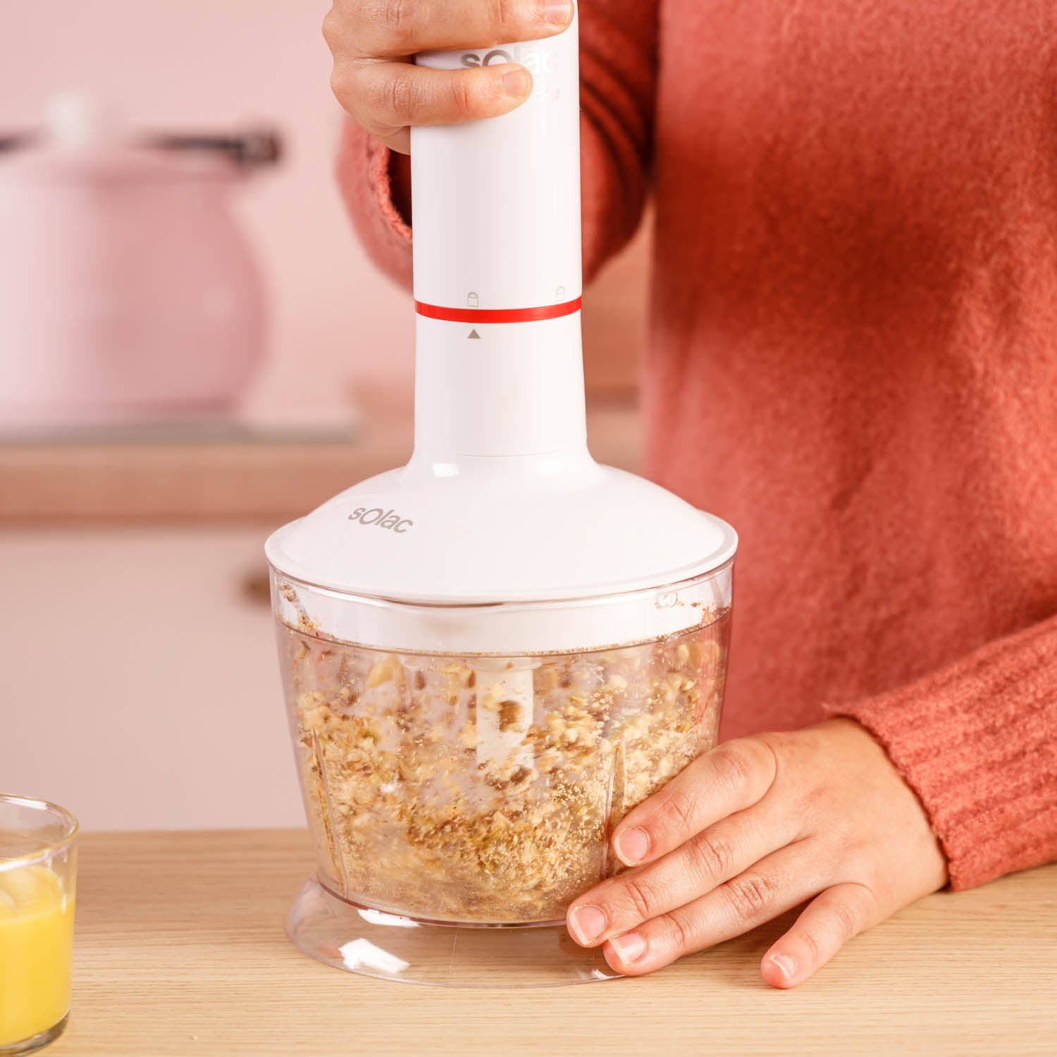 Dłoń trzyma biały blender ręczny nad przezroczystym pojemnikiem z jedzeniem.