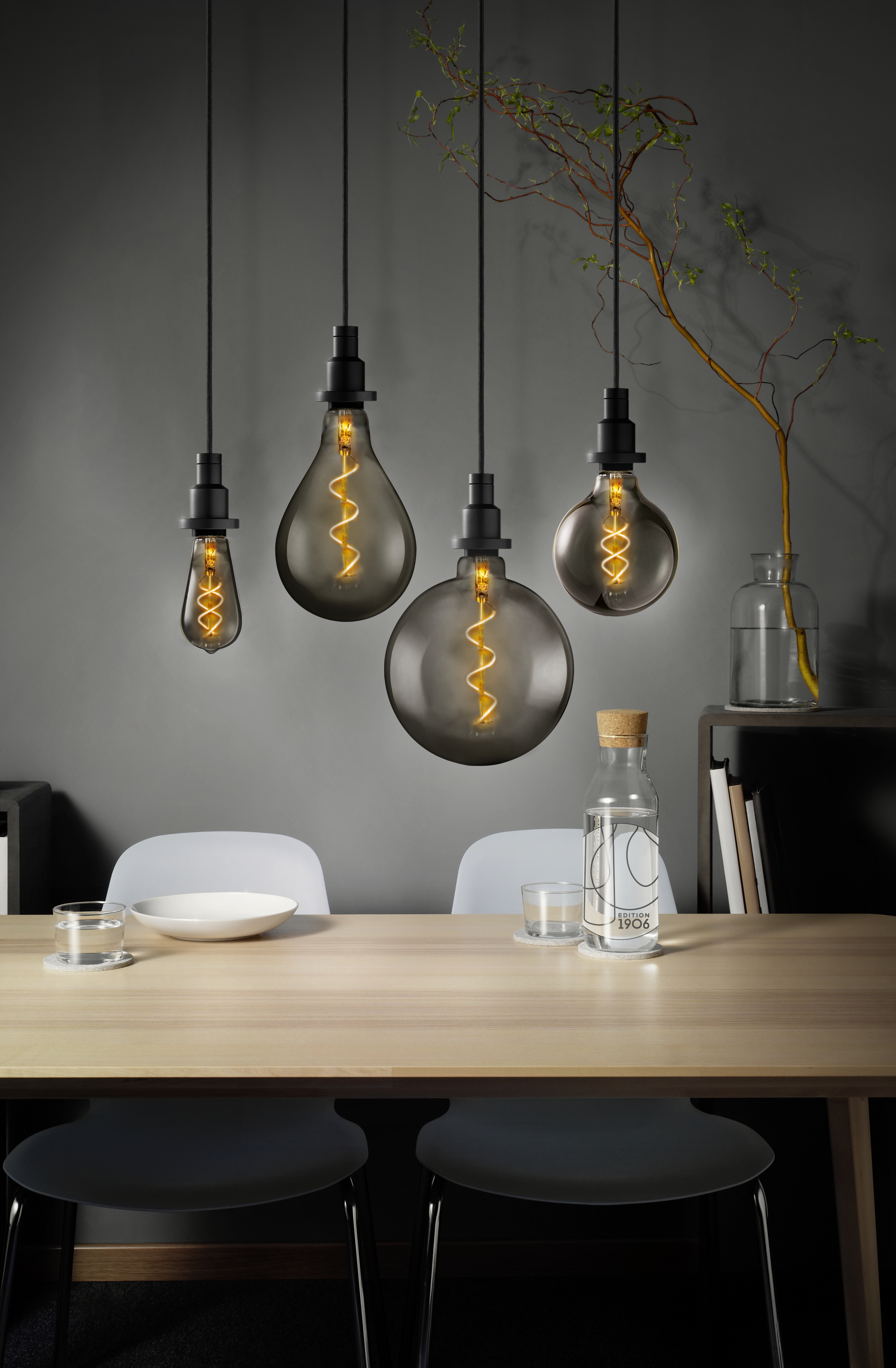 Quattro lampadine appese sopra un tavolo di legno. Una ha una forma a goccia, le altre sono rotonde.