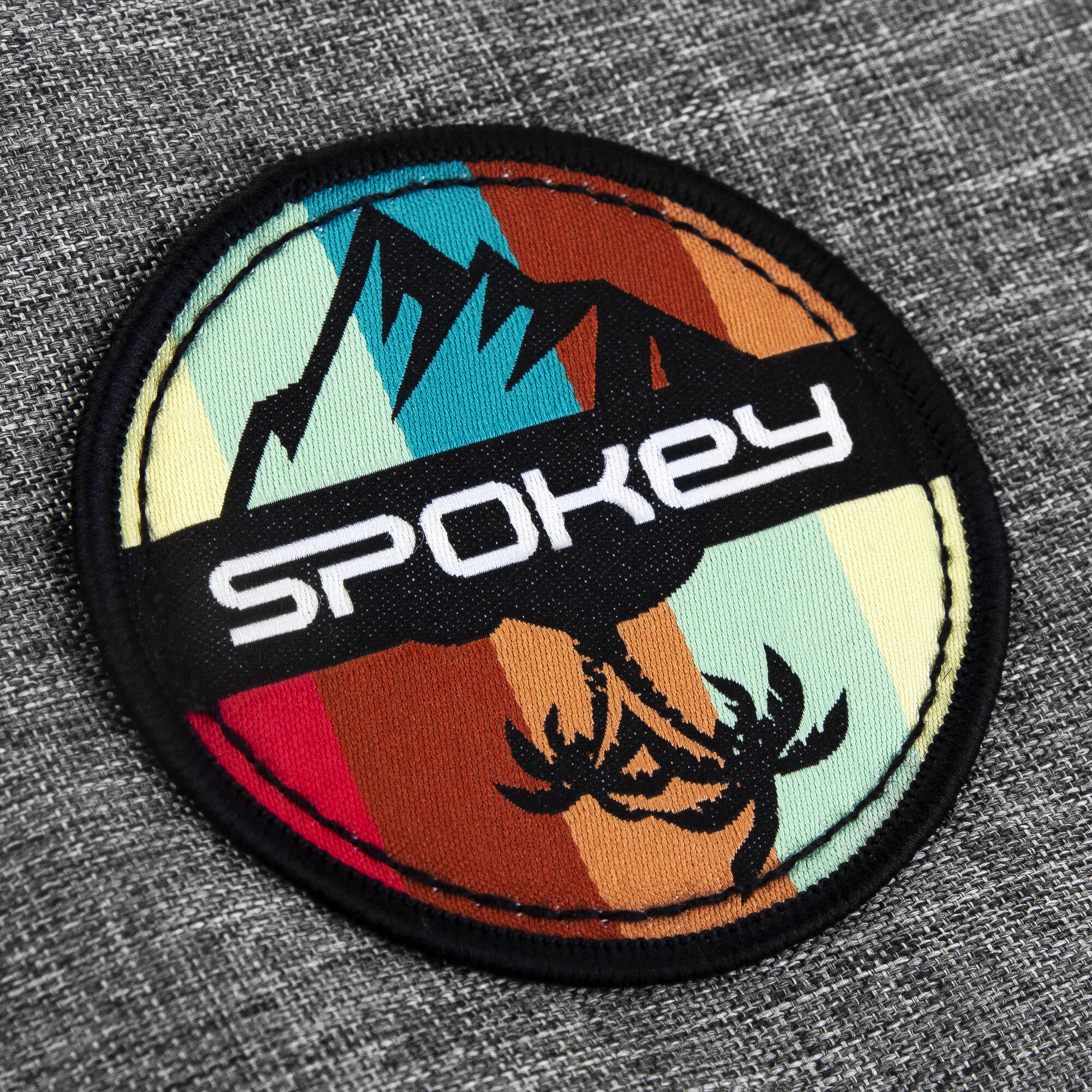 Zbliżenie na naszywkę Spokey z górą i palmami na szarej torbie.