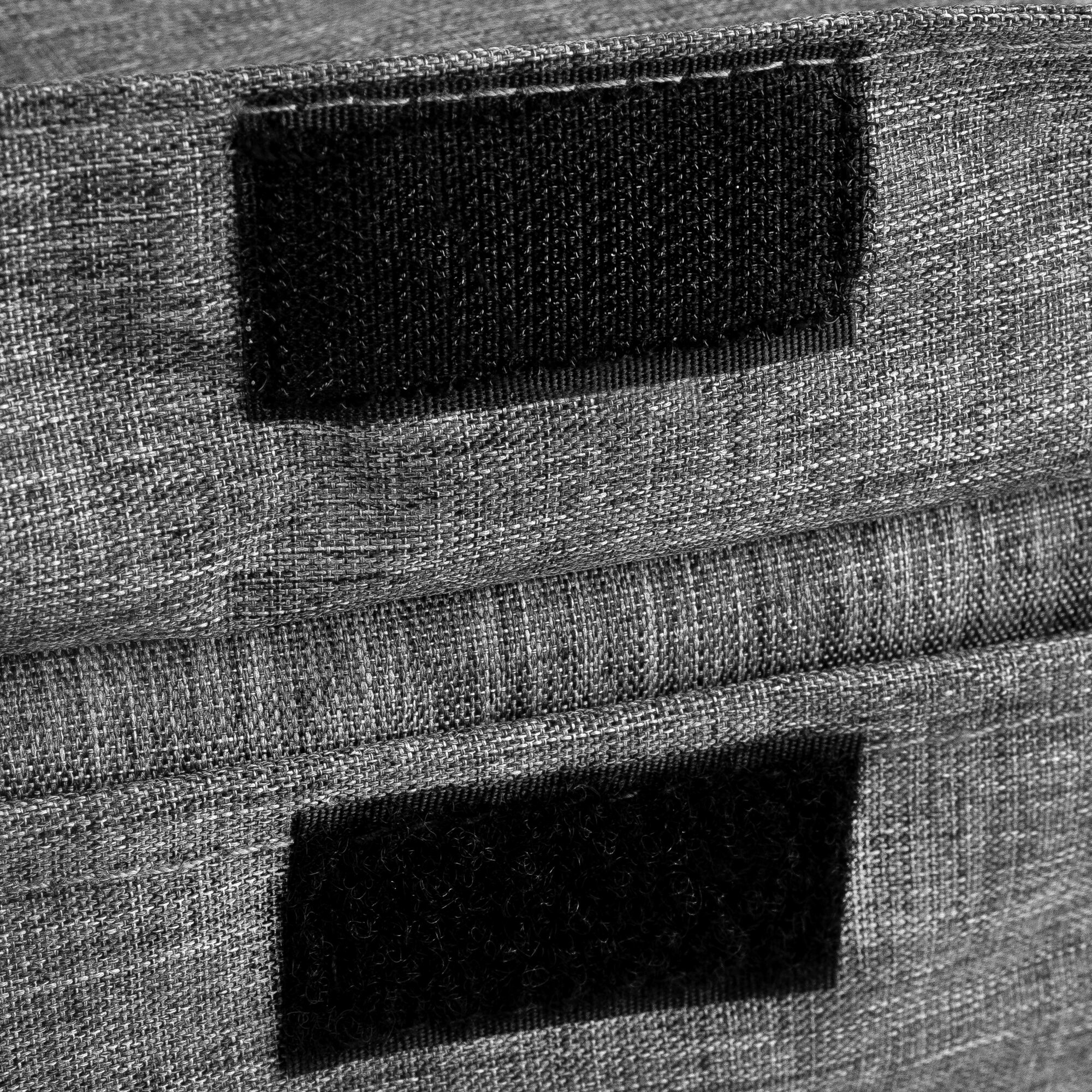 Zbliżenie dwóch czarnych naszywek na rzepy na szarej tkaninie.