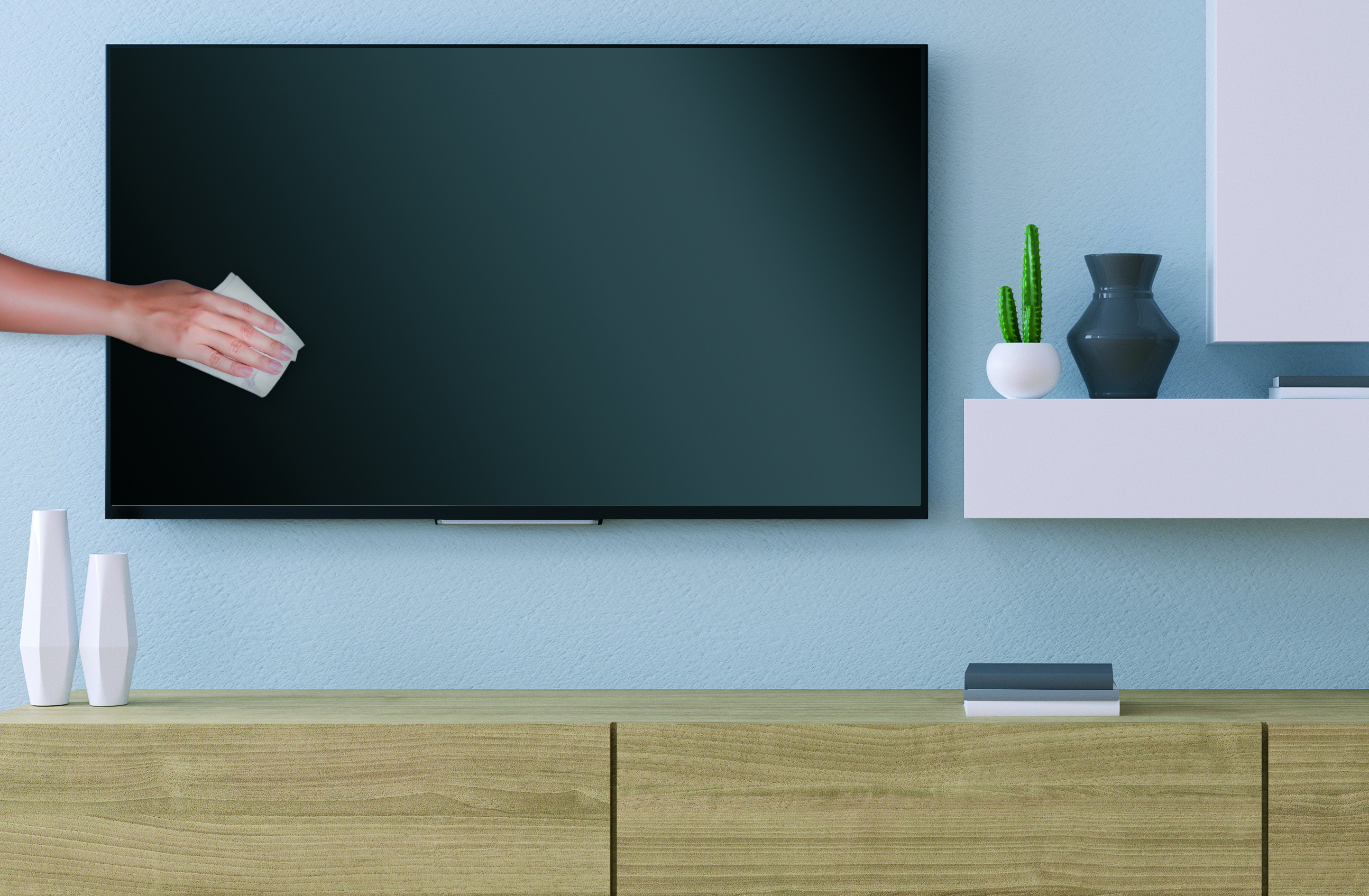 Una mano pulisce un televisore a schermo piatto montato su una parete azzurra sopra un mobile in legno. C'è una pianta e un vaso.