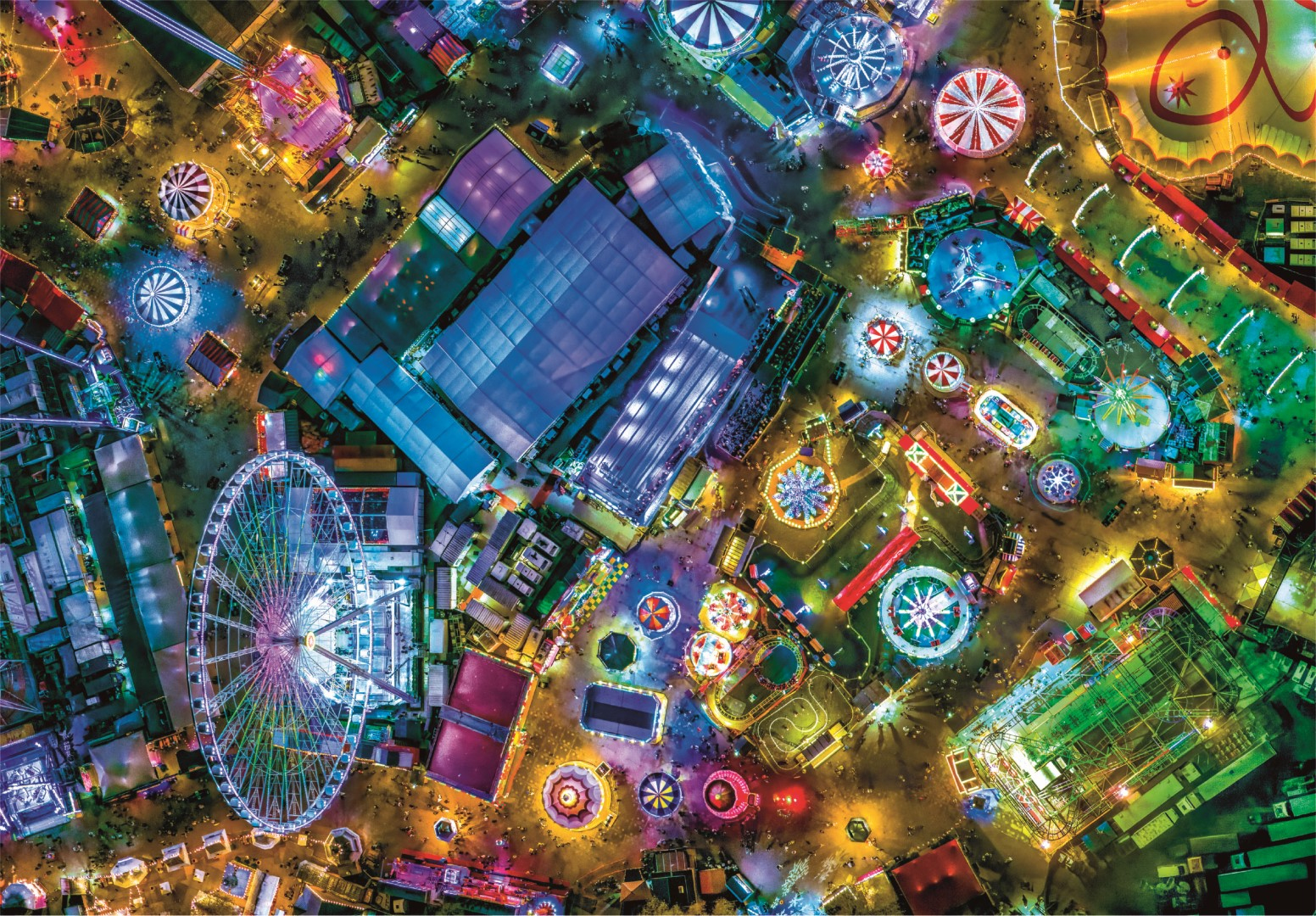 Widok z lotu ptaka na jasno oświetlony park rozrywki w nocy, z diabelskim młynem i kolejkami górskimi.