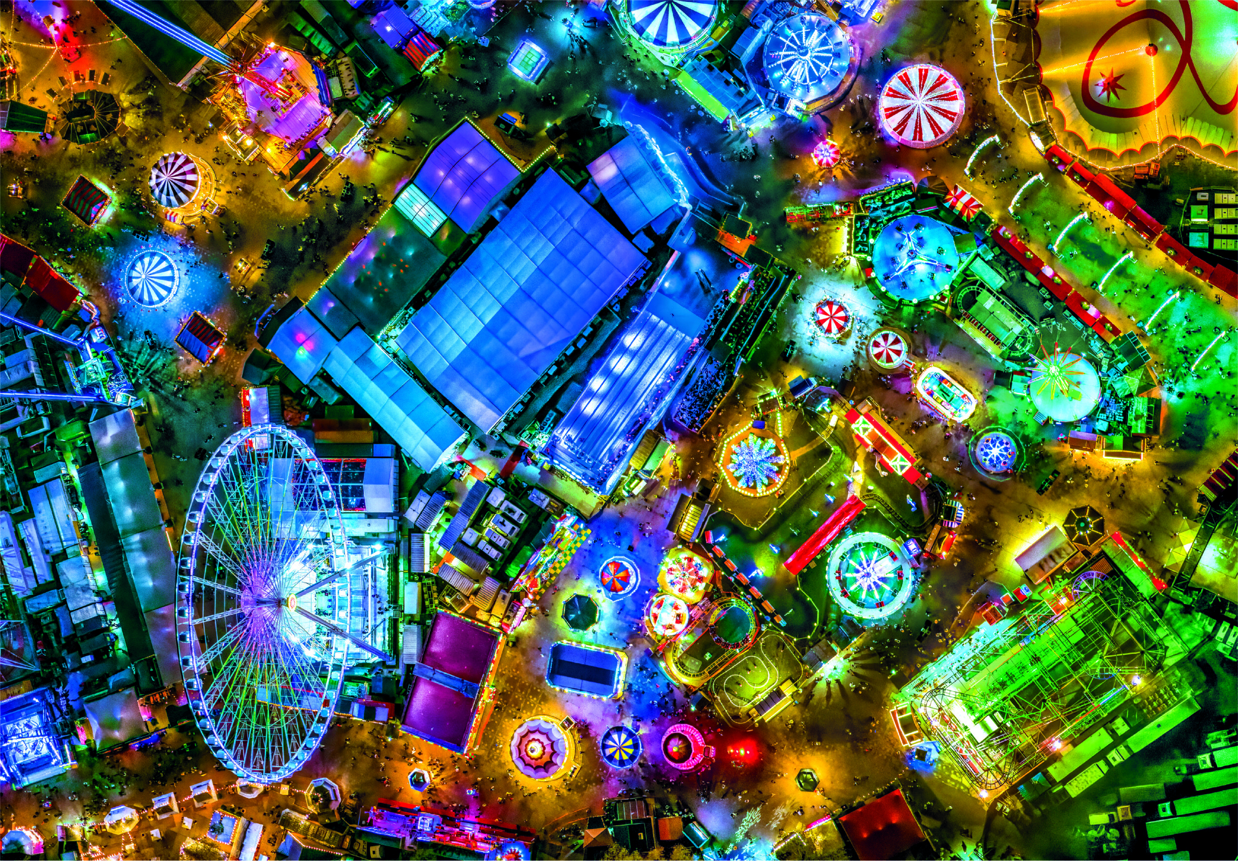 Widok z lotu ptaka na jasno oświetlony park rozrywki w nocy, z diabelskim młynem i kolejkami górskimi.