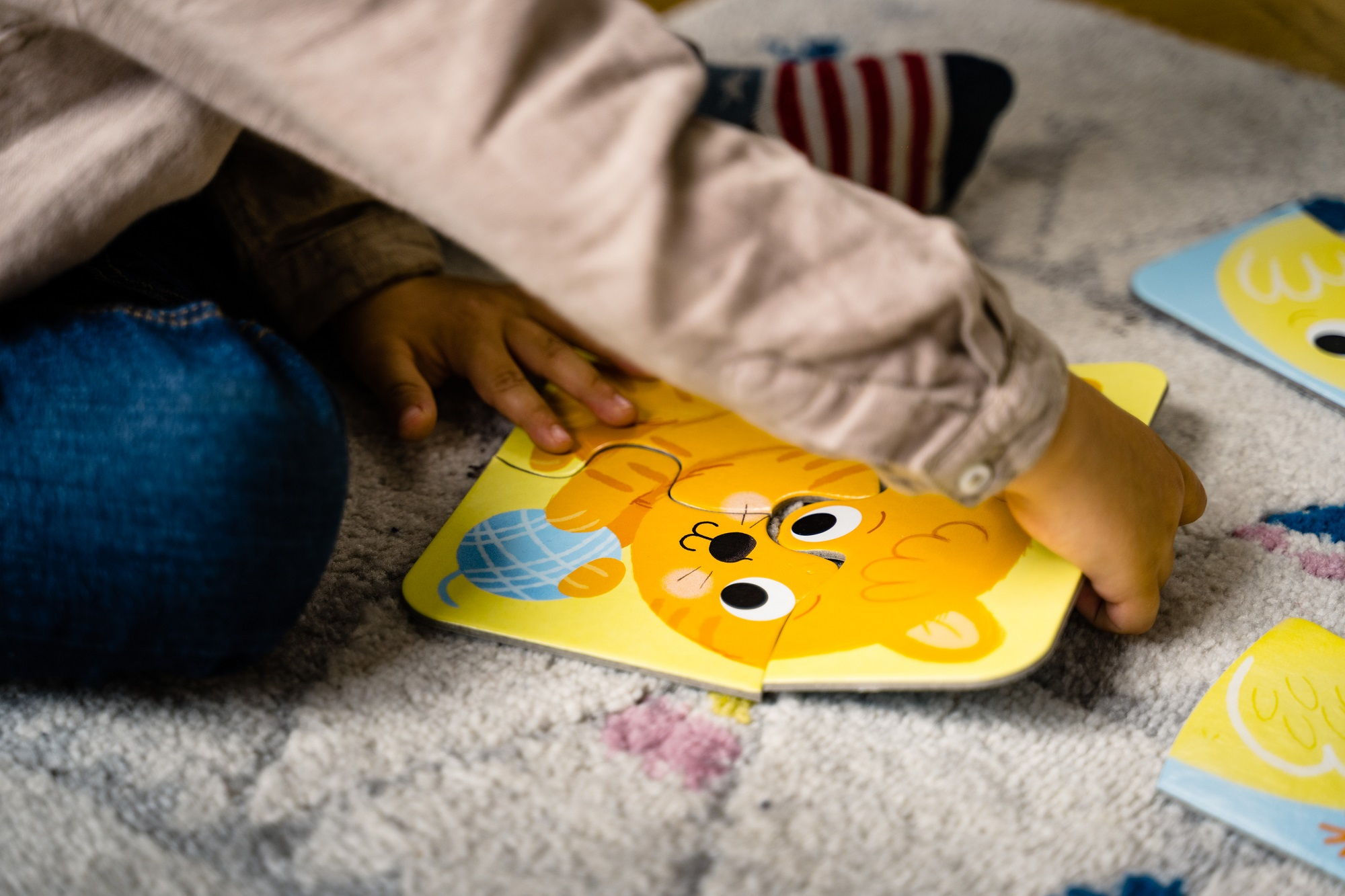 Ręka dziecka umieszcza element układanki z kotem na żółtym tle. Układanka jest prawie gotowa.