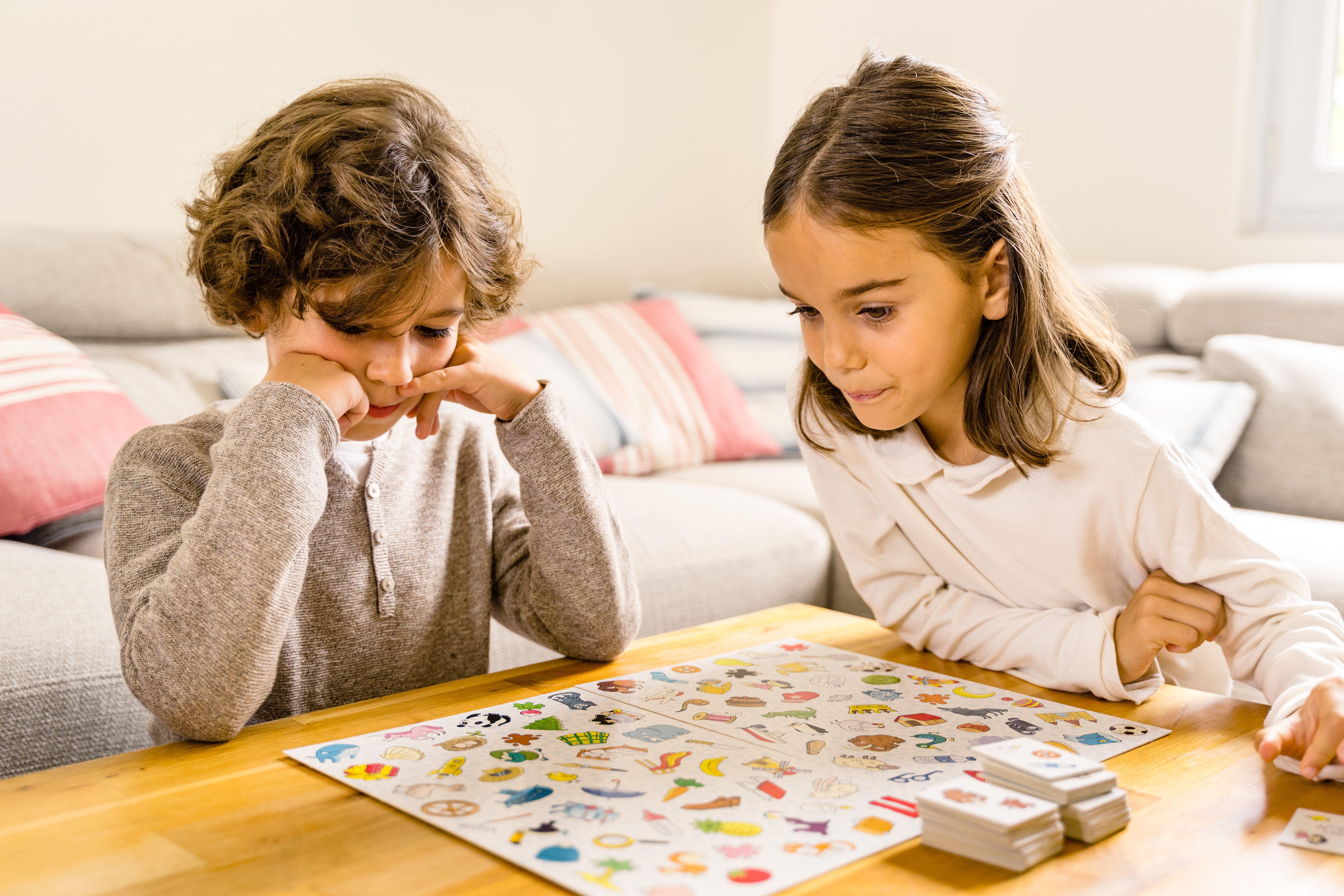 Due bambini giocano a un gioco da tavolo su un tavolo di legno. I pezzi del gioco sono visibili.