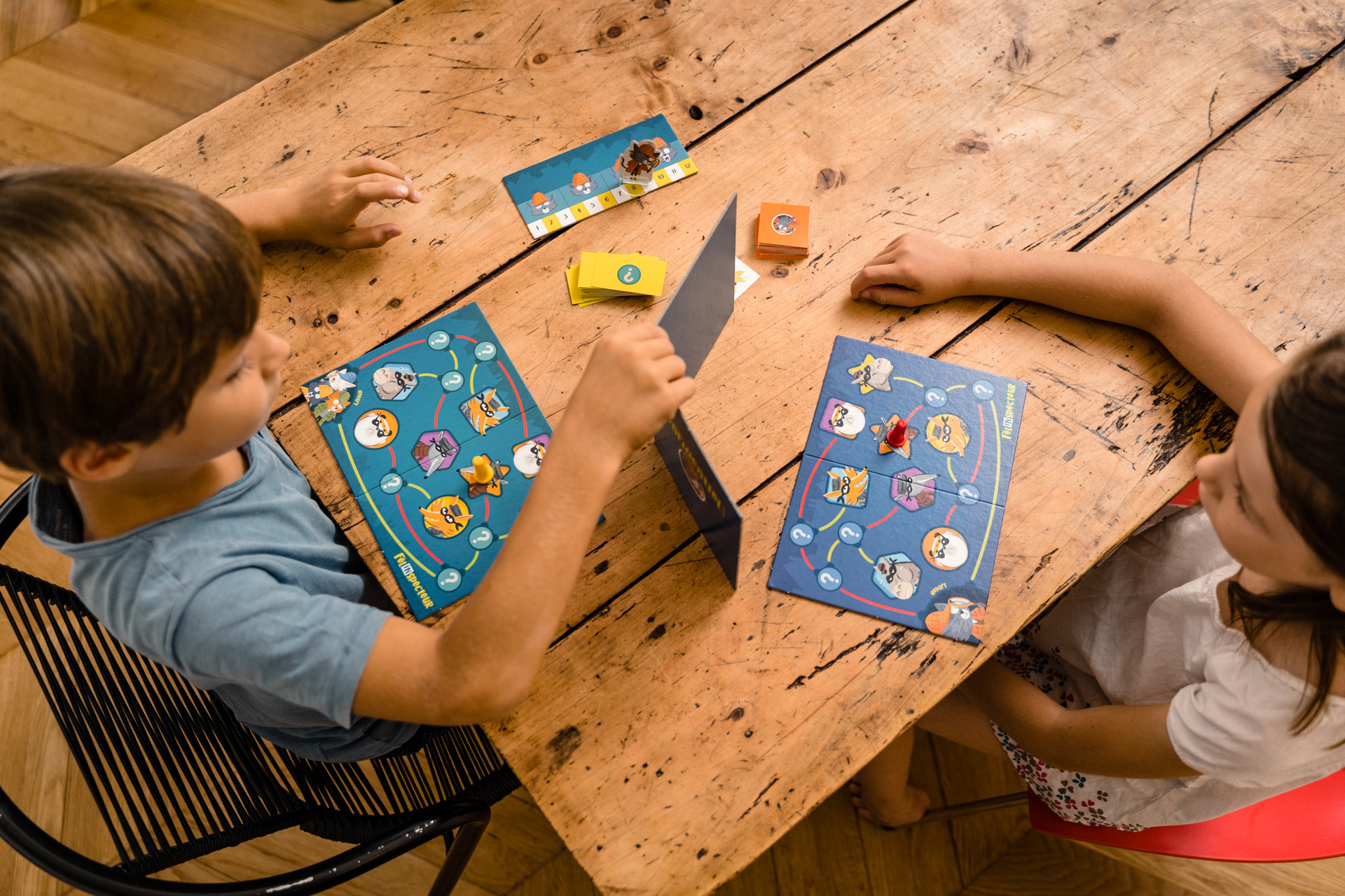 Zwei Kinder spielen ein Brettspiel auf einem Holztisch.
