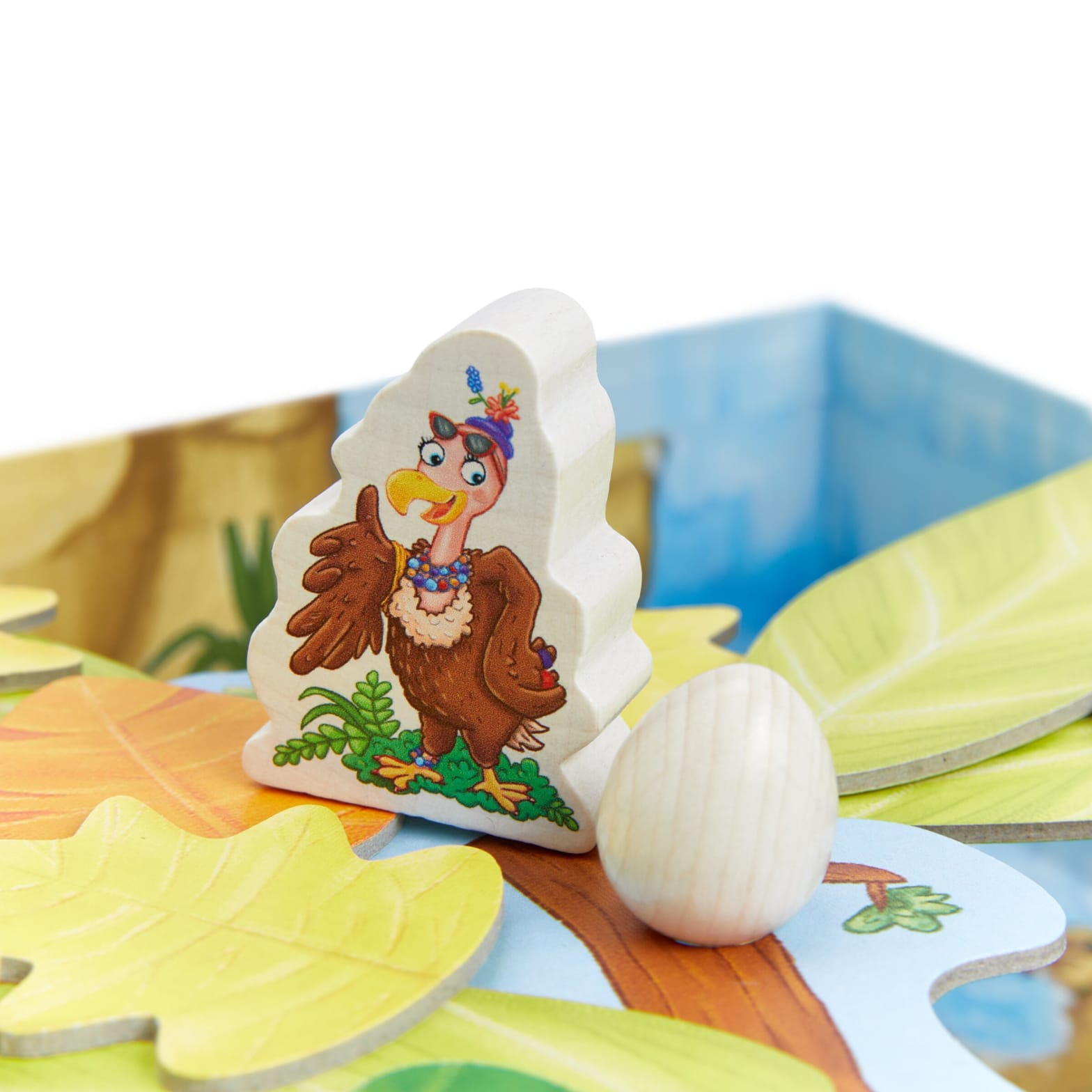 Pièce de jeu en bois d'un oiseau portant un chapeau, à côté d'un œuf et de feuilles.
