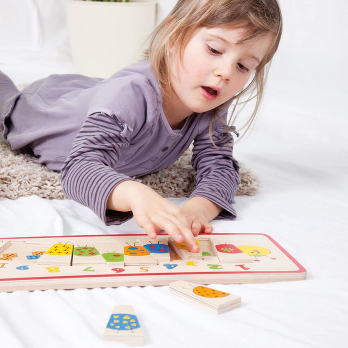 Una niña jugando con un rompecabezas de madera. Está buscando una pieza del rompecabezas en la tabla de madera.