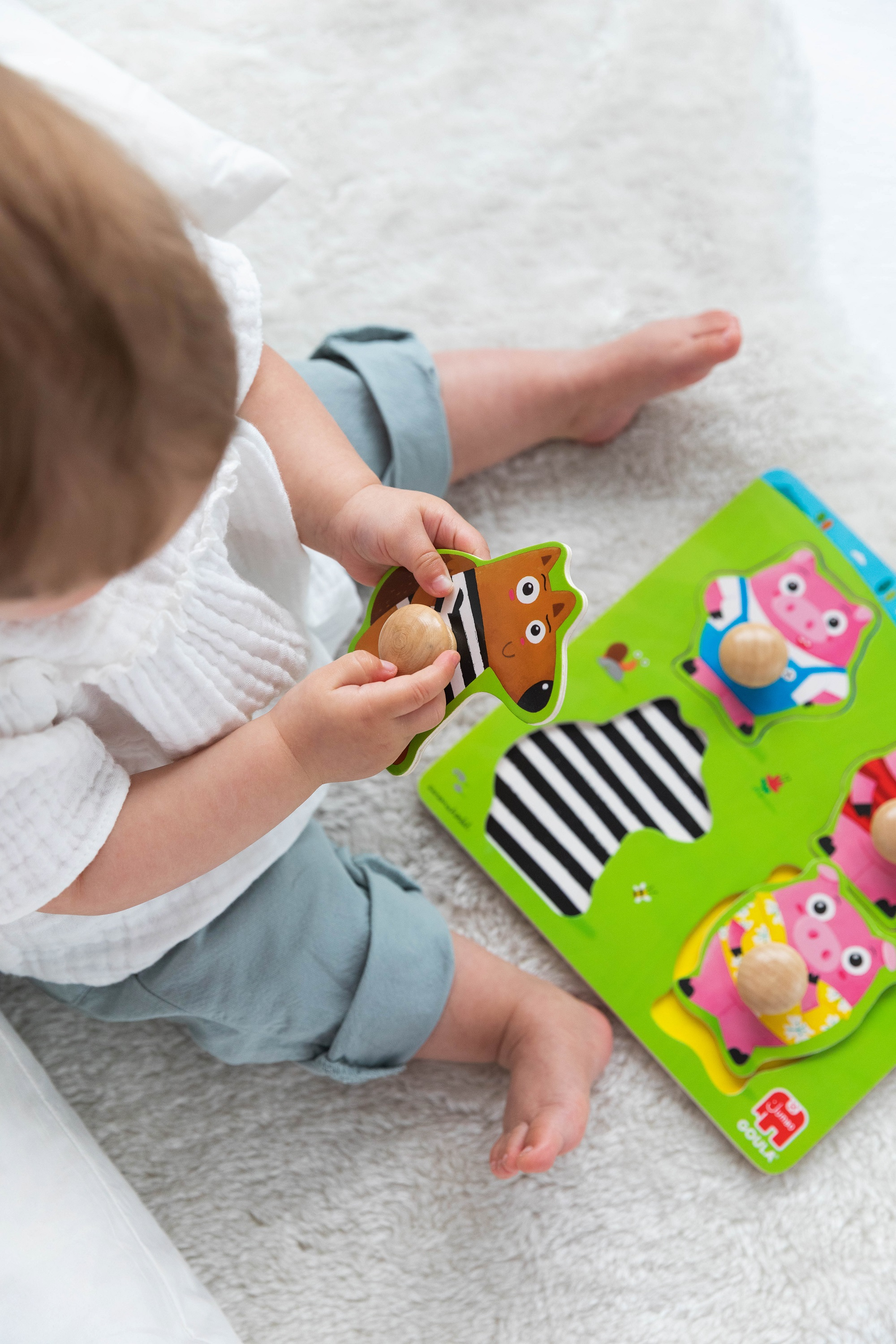 Niemowlę bawi się drewnianą układanką z kształtami zwierząt. Układanka jest zielona.