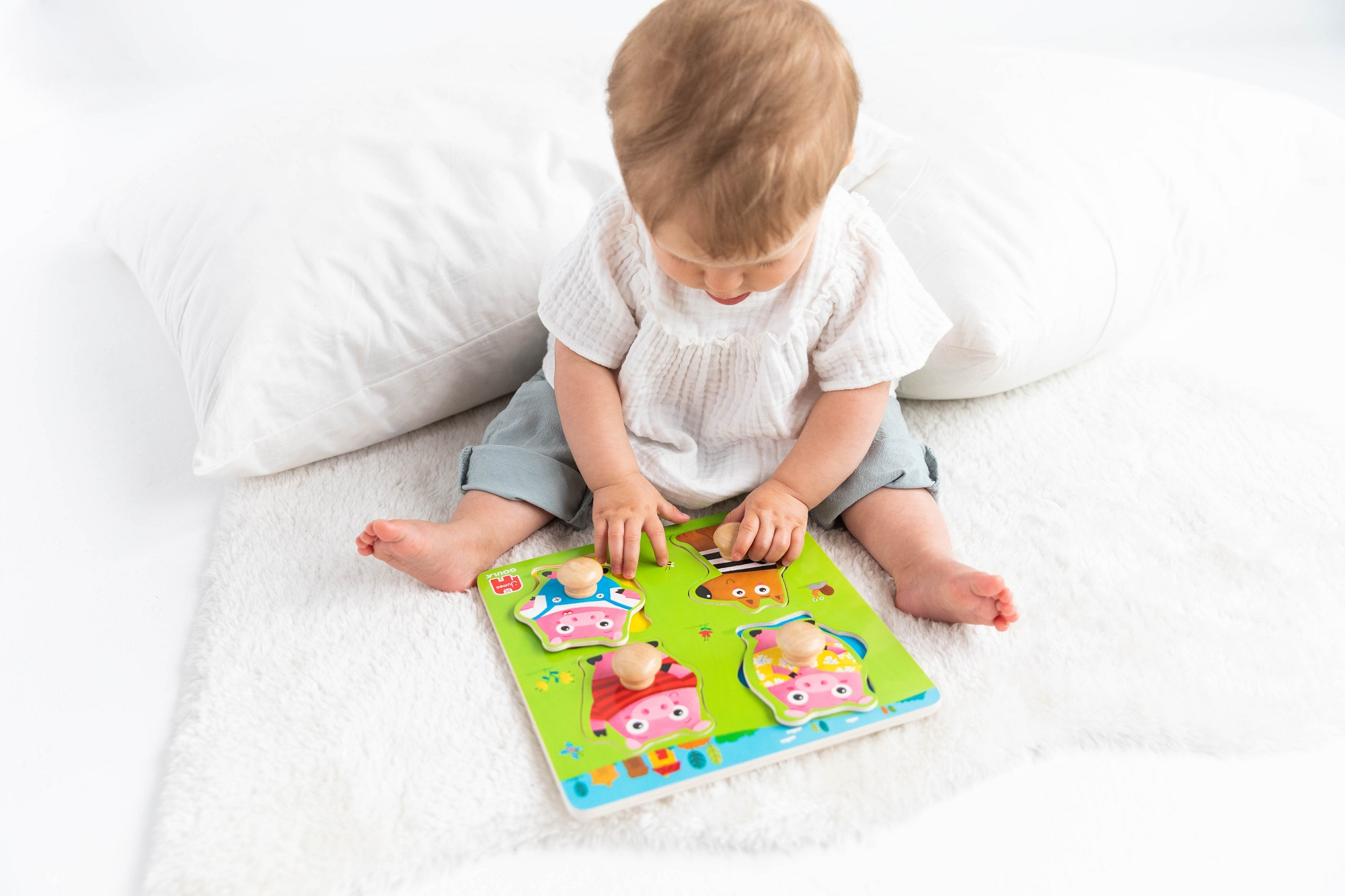 Niemowlę bawi się puzzlami na białym, puszystym dywanie. Puzzle przedstawiają domy.