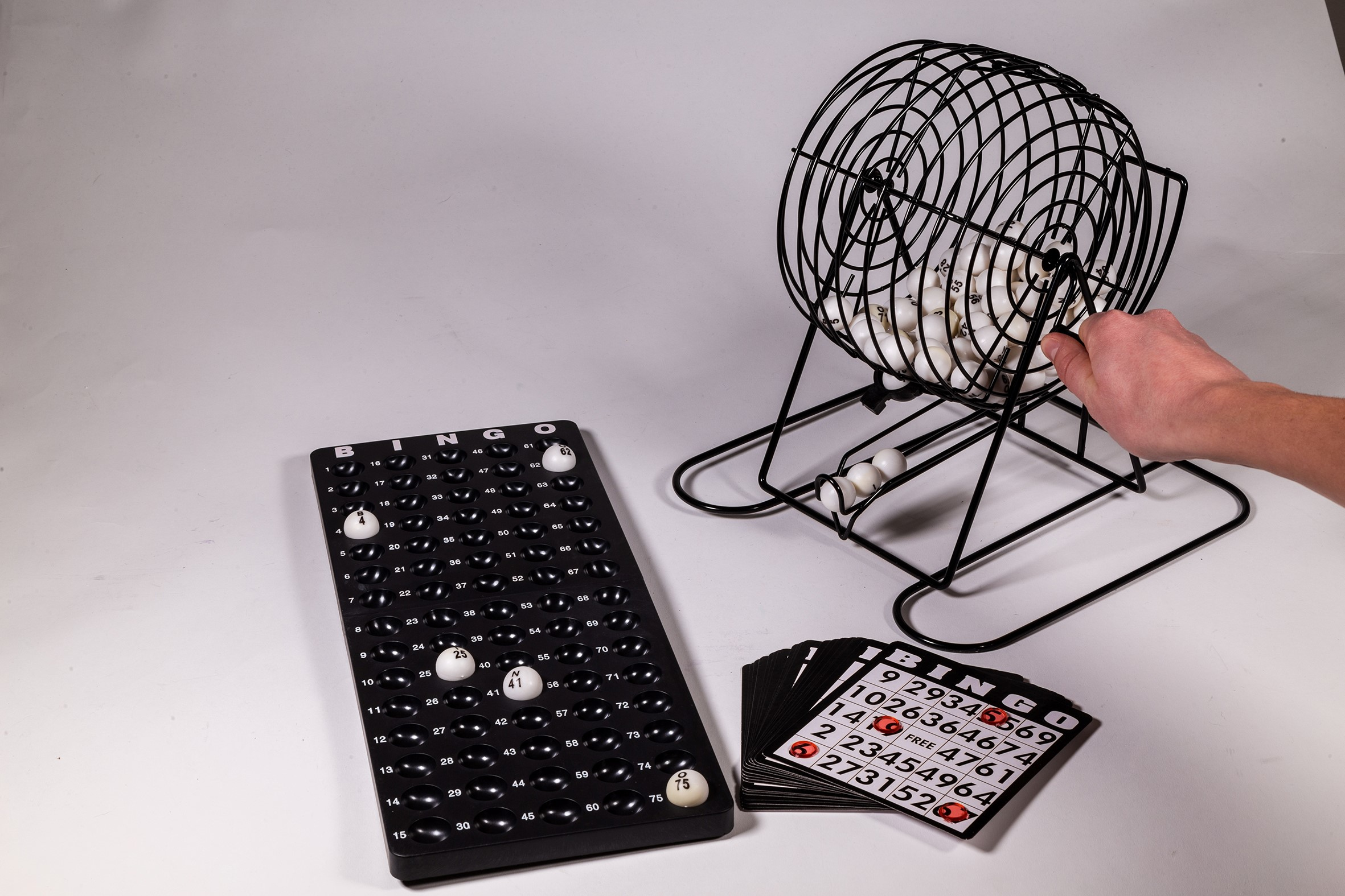 Un set di bingo con una gabbia rotante, cartelle del bingo e palline numerate su una superficie bianca.