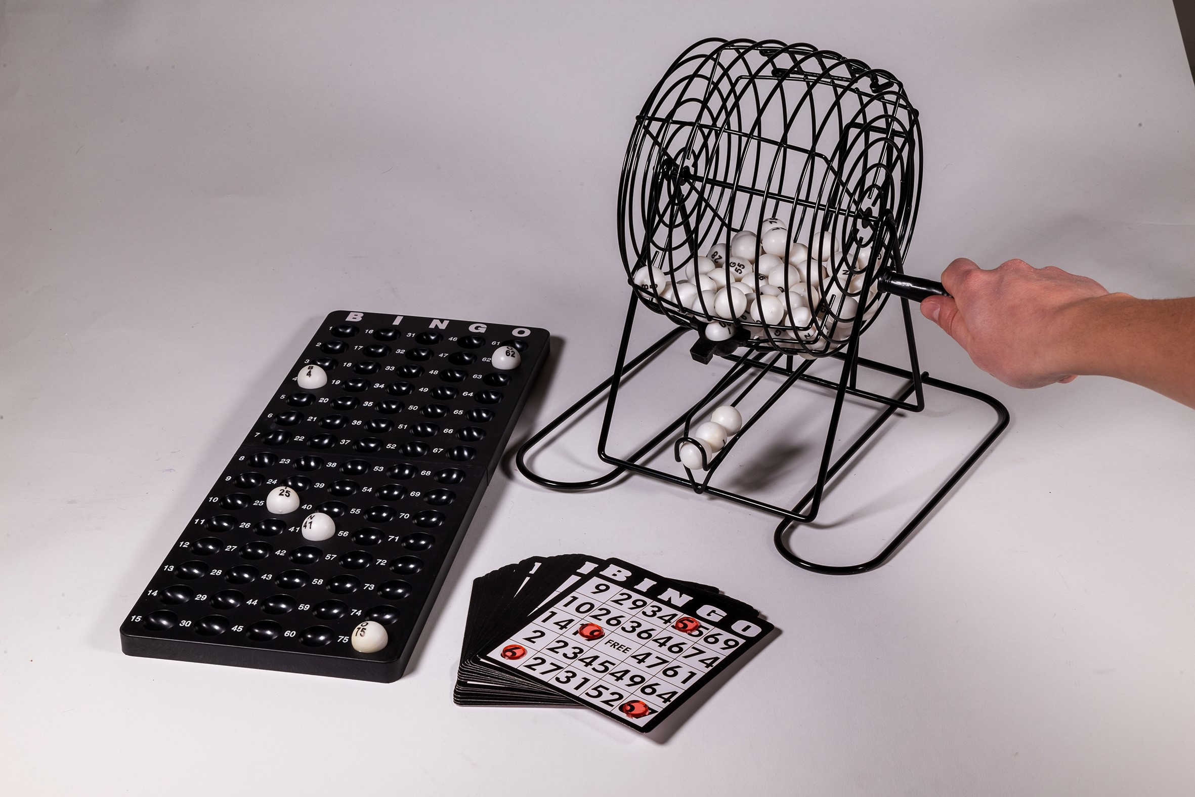 Un set di bingo con gabbia, palline numerate, cartelle e un vassoio. Una mano gira la gabbia.