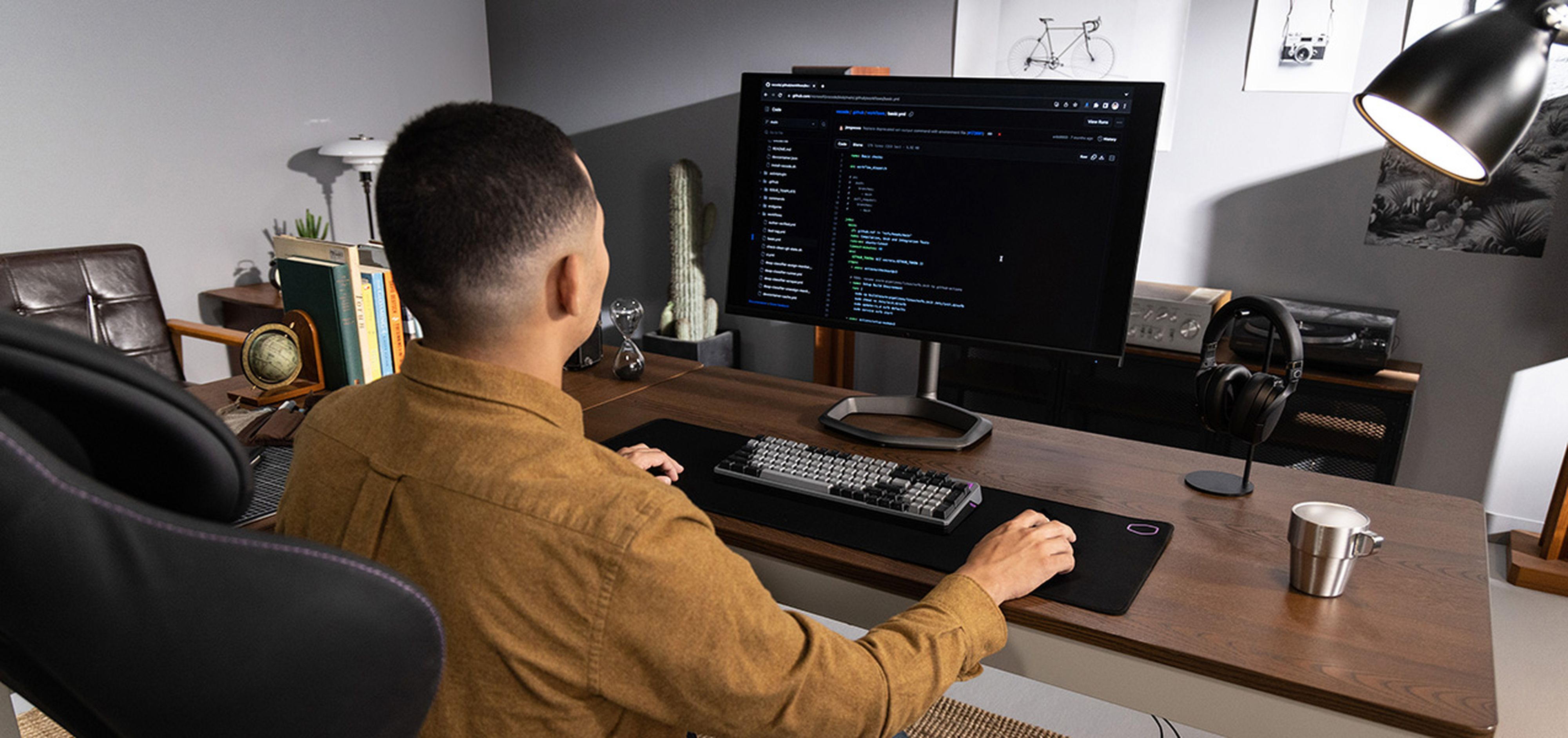 Uomo che lavora a una scrivania con monitor e tastiera. La scrivania ha un tappetino per il mouse e cuffie.