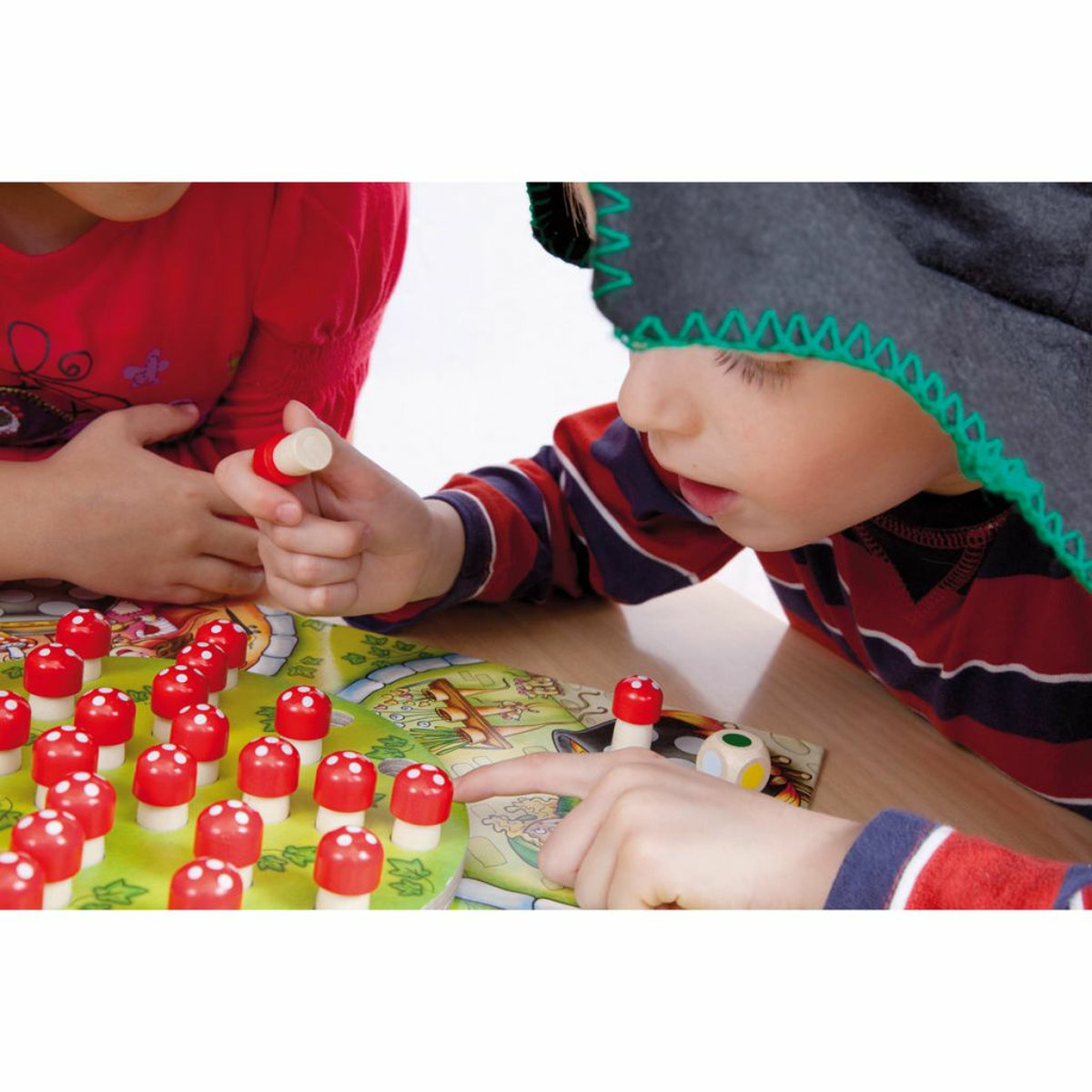 Zwei Kinder spielen ein Brettspiel mit roten Pilzfiguren auf einem grünen Brett.