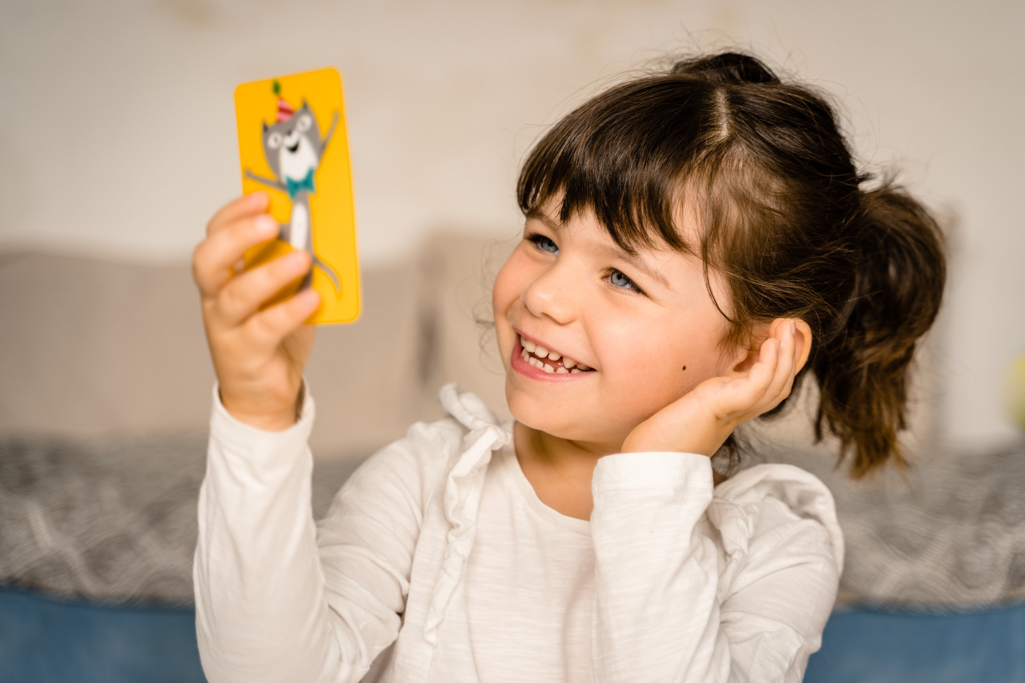 Mała dziewczynka uśmiecha się, patrząc na kartę z wilkiem z kreskówki. Trzyma ją w górze.