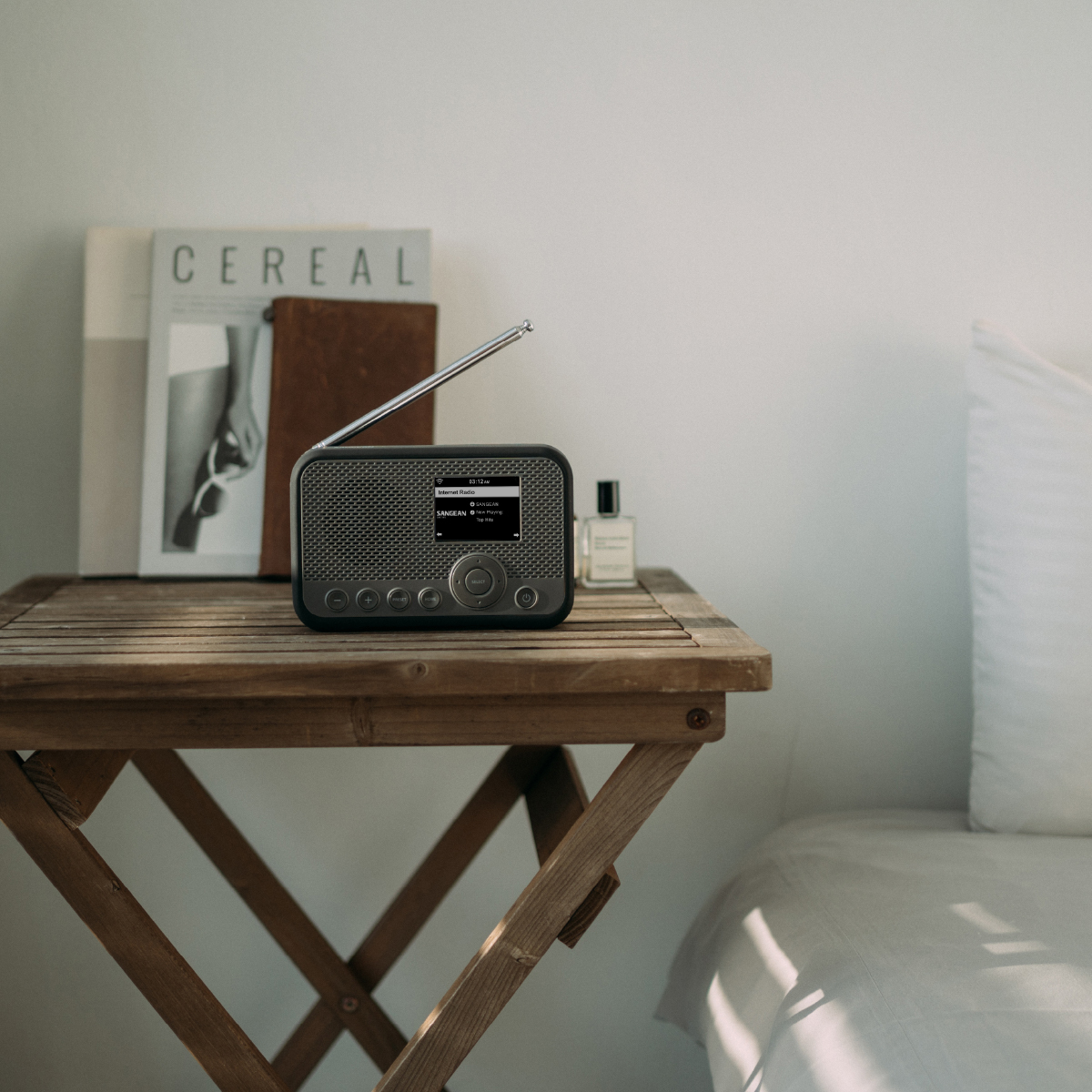Małe radio na stoliku obok książki i łóżka.