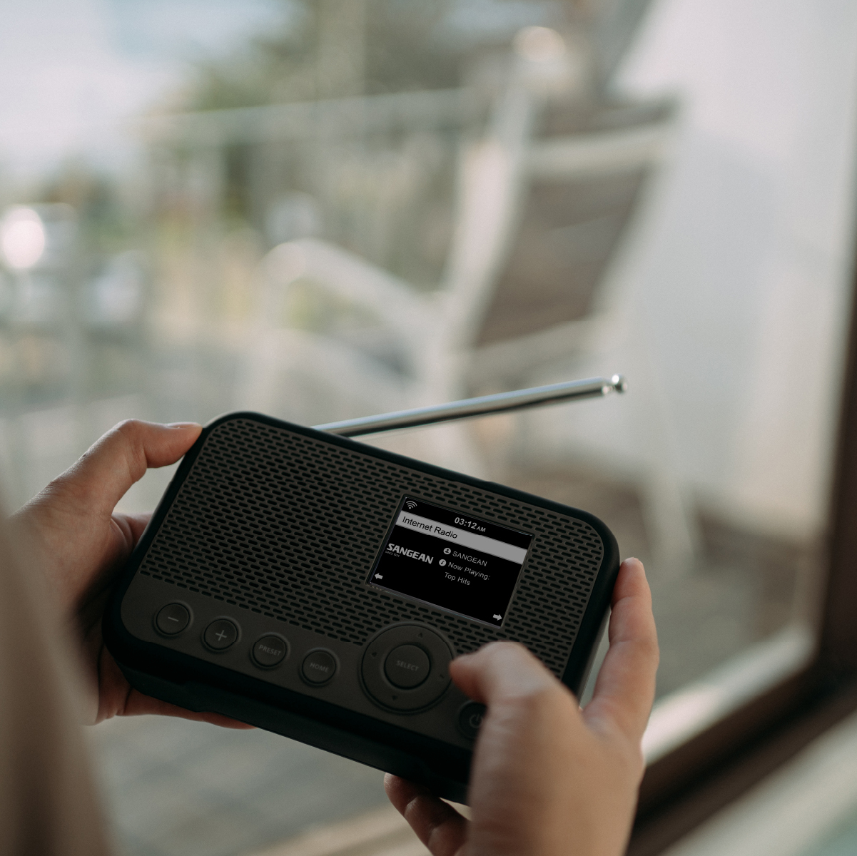 Dłonie trzymające czarne radio z ekranem wyświetlającym czas i informacje o stacji. Tło zewnętrzne.