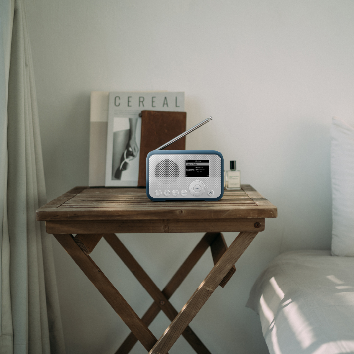 Radio na drewnianym stoliku obok łóżka. Obecny jest również magazyn i perfumy.