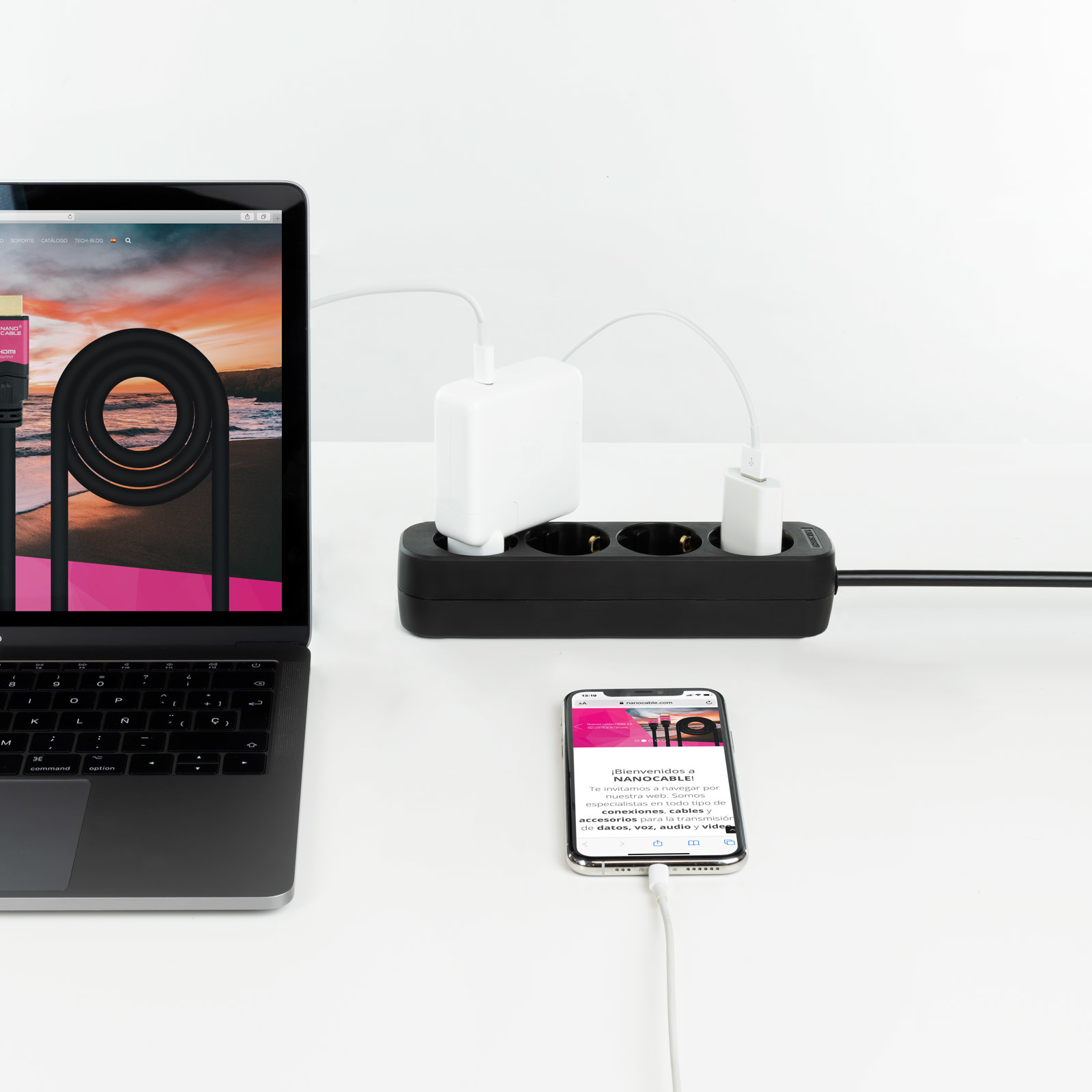 Laptop, telefoon opladen via een zwarte stekkerdoos. Witte muur.
