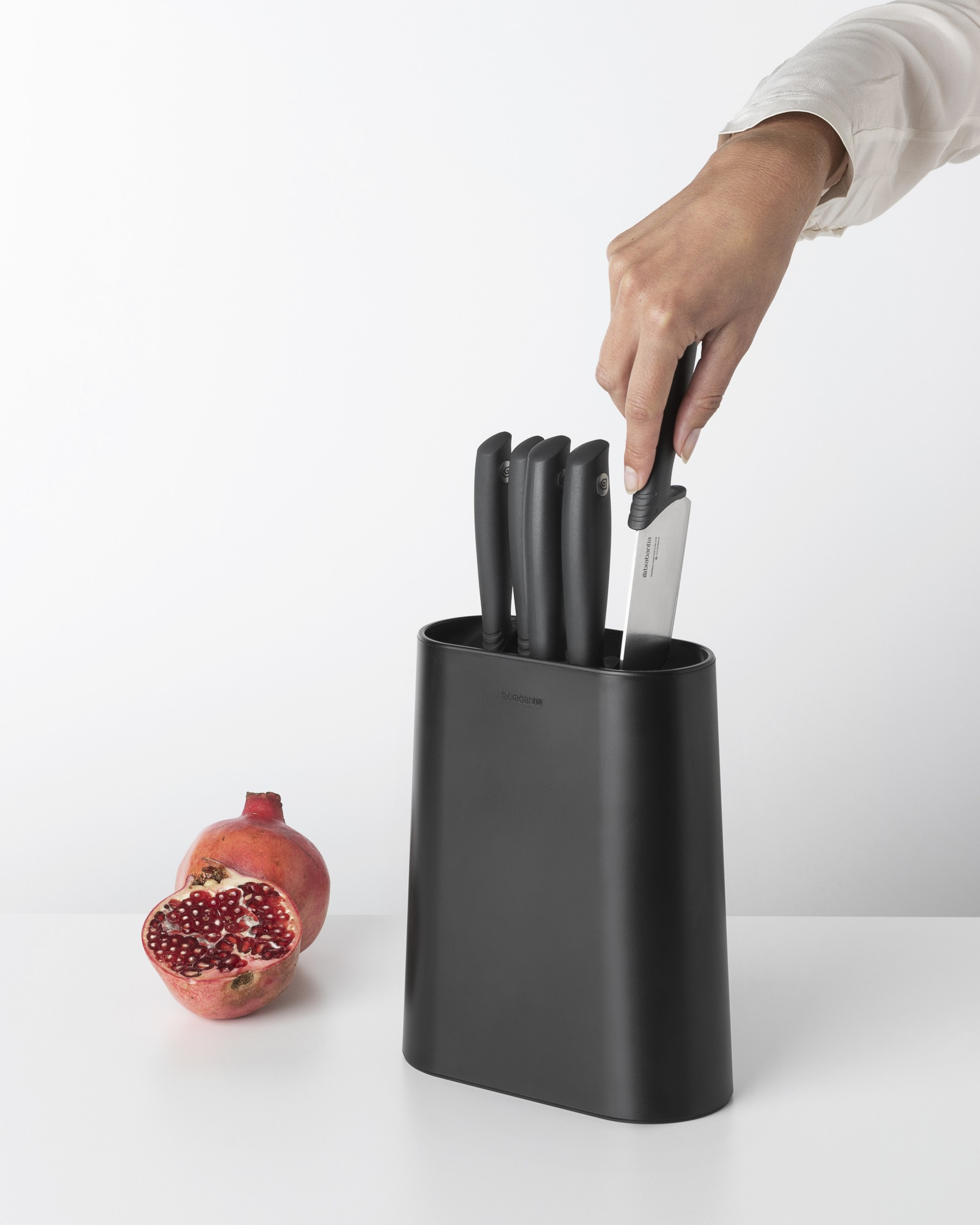Eine Hand legt ein Messer in einen schwarzen Messerblock, mit einem Granatapfel.
