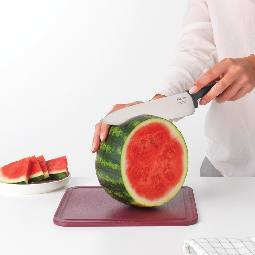 Kobieta kroi arbuza na czerwonej desce, plasterki na talerzu.