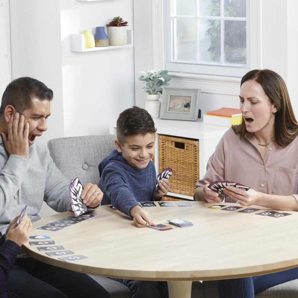 Een gezin van vier kaarten aan een ronde tafel. Gezichten tonen verbazing en opwinding.