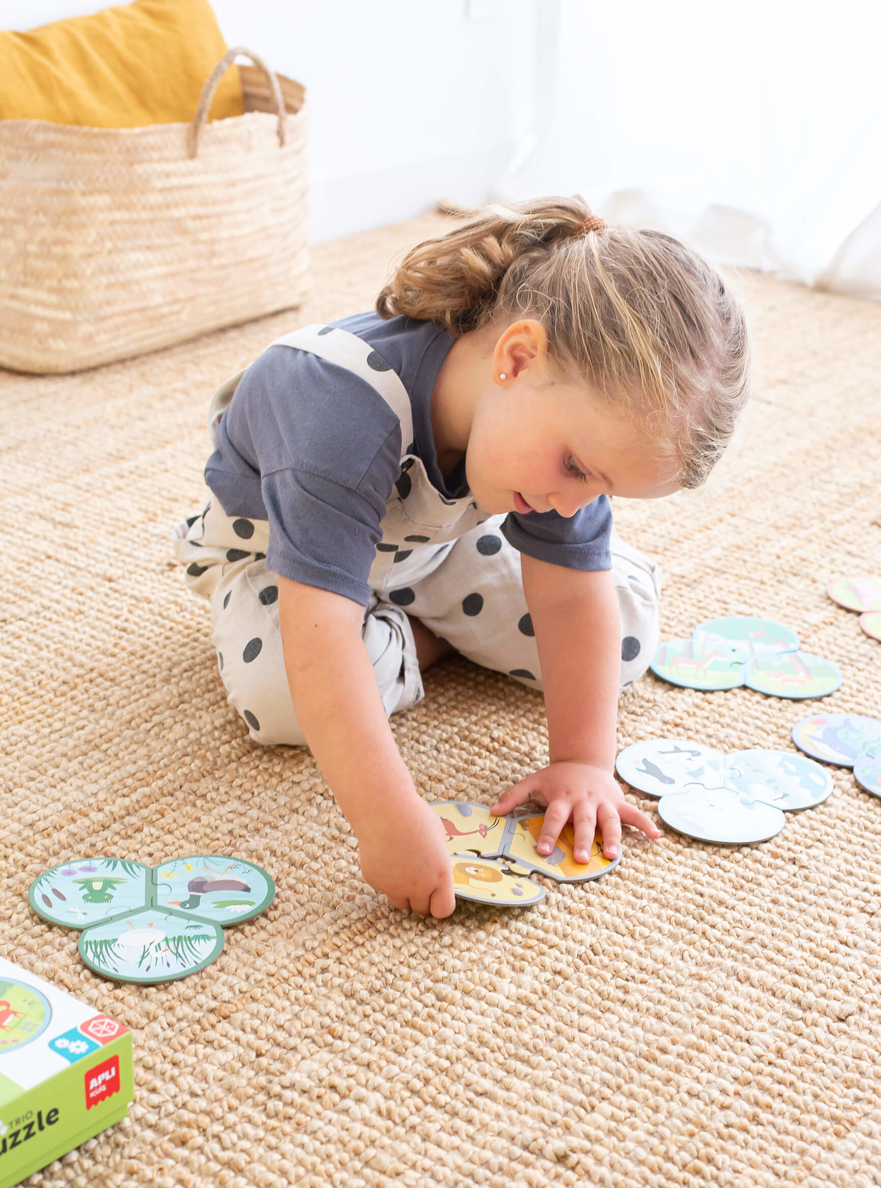 Niña jugando con un rompecabezas sobre una alfombra. El rompecabezas tiene forma redonda con diferentes imágenes de animales.