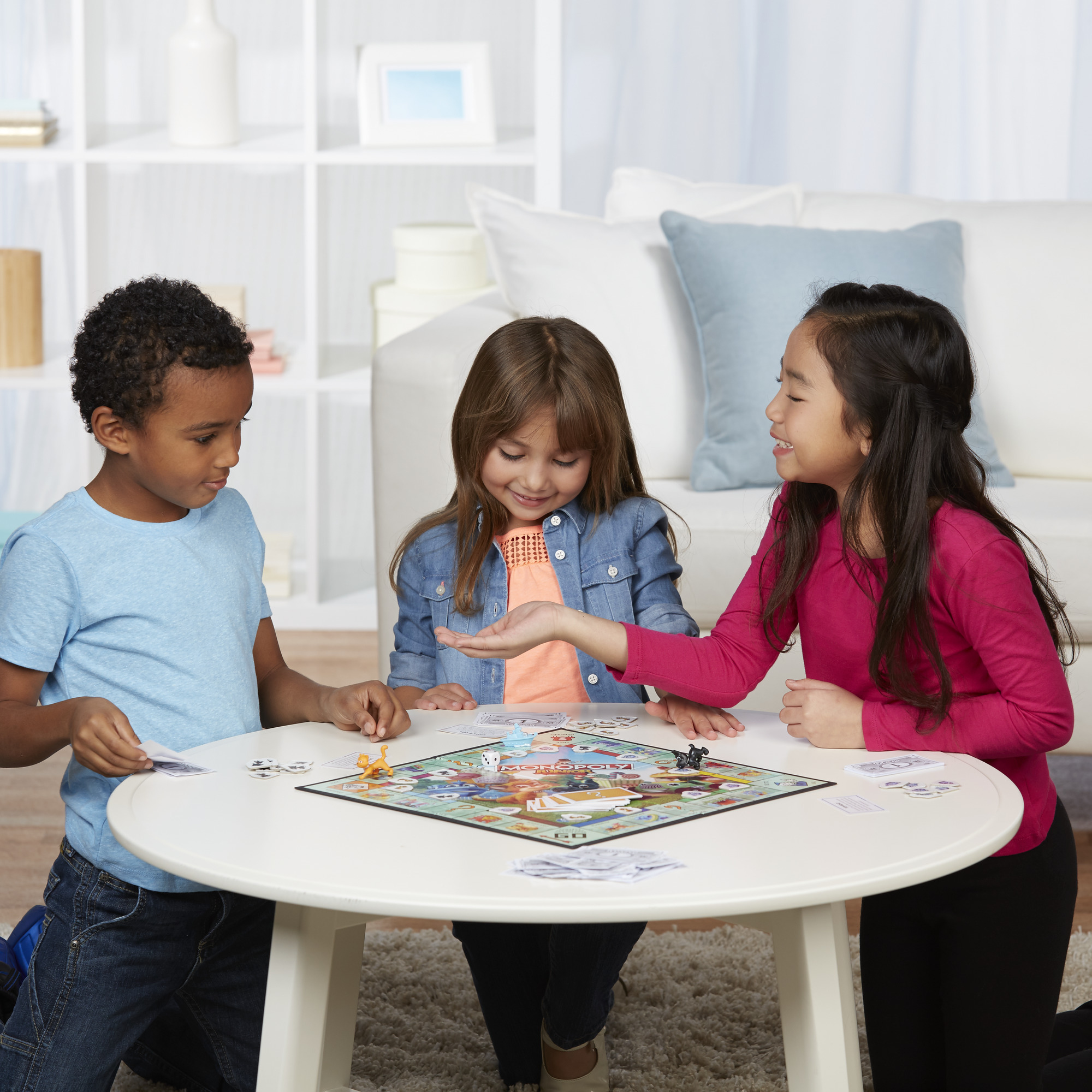 Drei Kinder spielen Monopoly Junior. Sie sitzen um einen Tisch mit dem Spielbrett und den Spielsteinen.