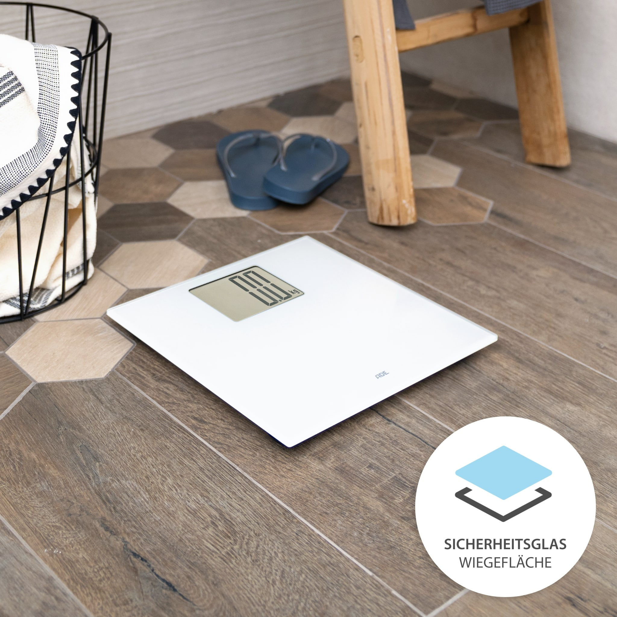 Bilancia da bagno digitale bianca su pavimento in legno, con asciugamano e infradito sullo sfondo.
