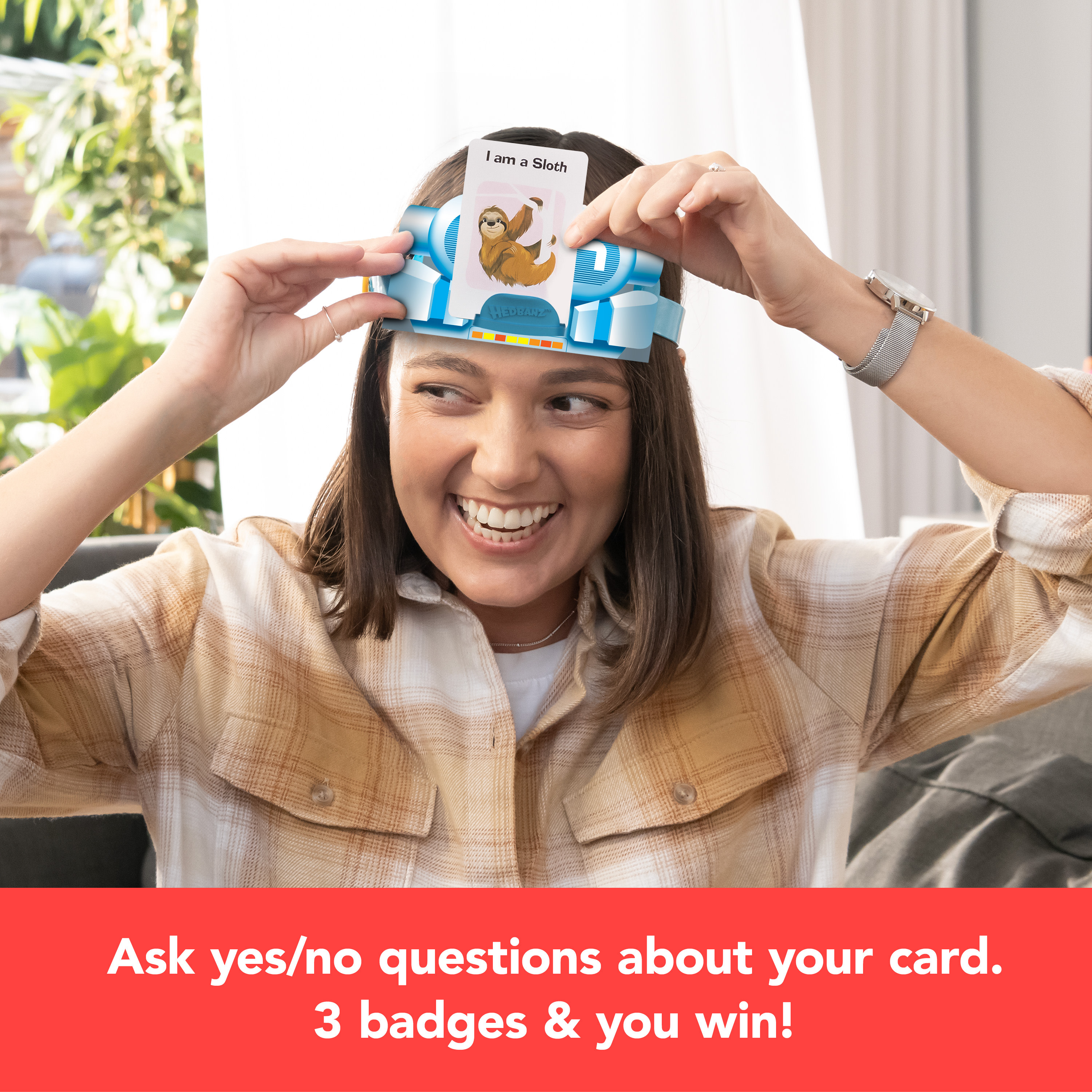 Uśmiechnięta kobieta, w nakryciu głowy Hedbanz, trzyma kartę, tekst: 'Zadawaj pytania tak/nie'.