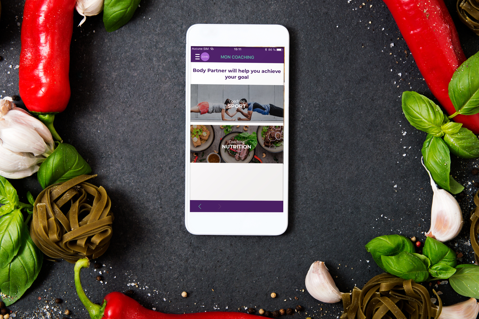Smartfon wyświetlający interfejs aplikacji fitness. Otoczony warzywami, przyprawami i makaronem.