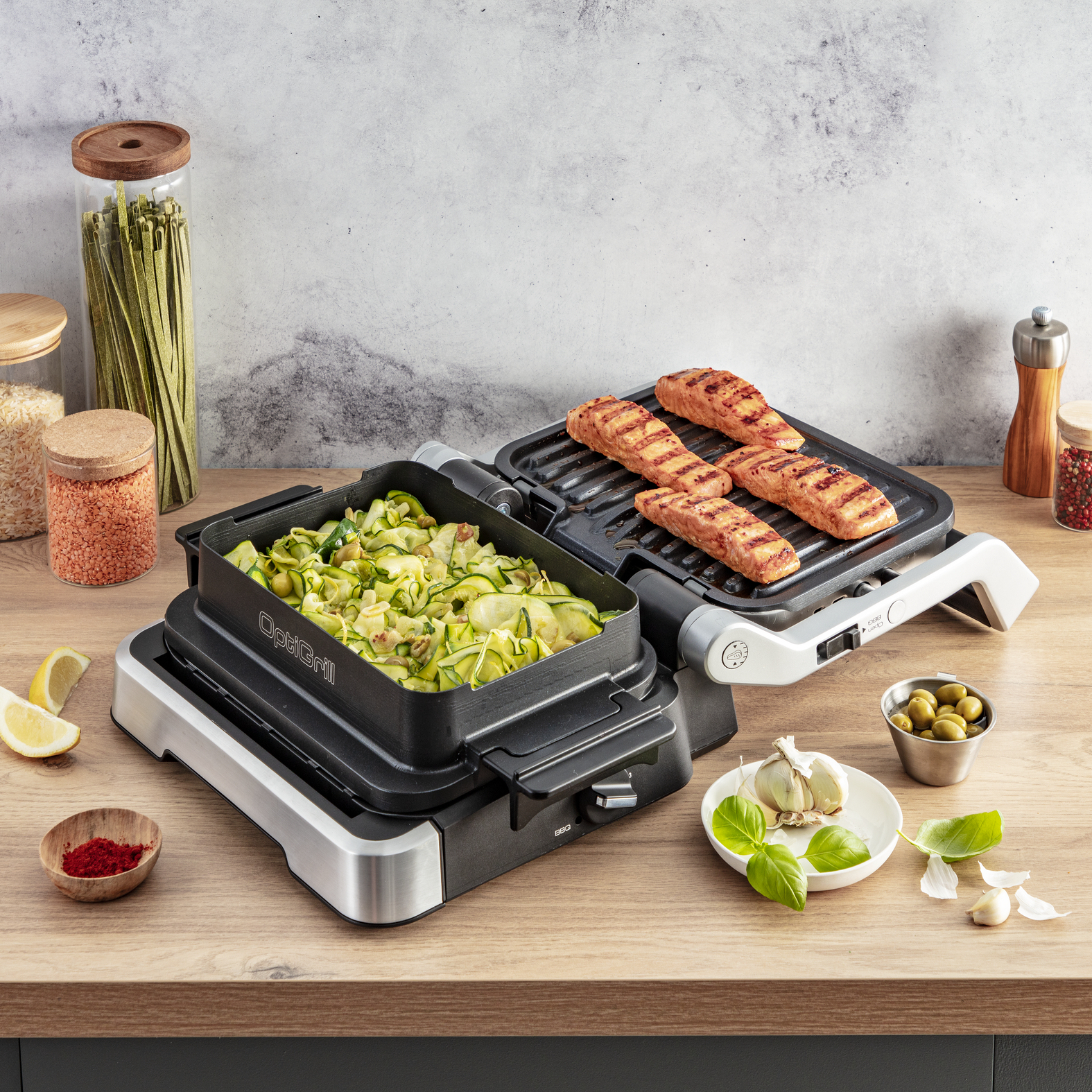 Elektrischer Grill mit Essen, daneben Zutaten, auf Holztisch.
