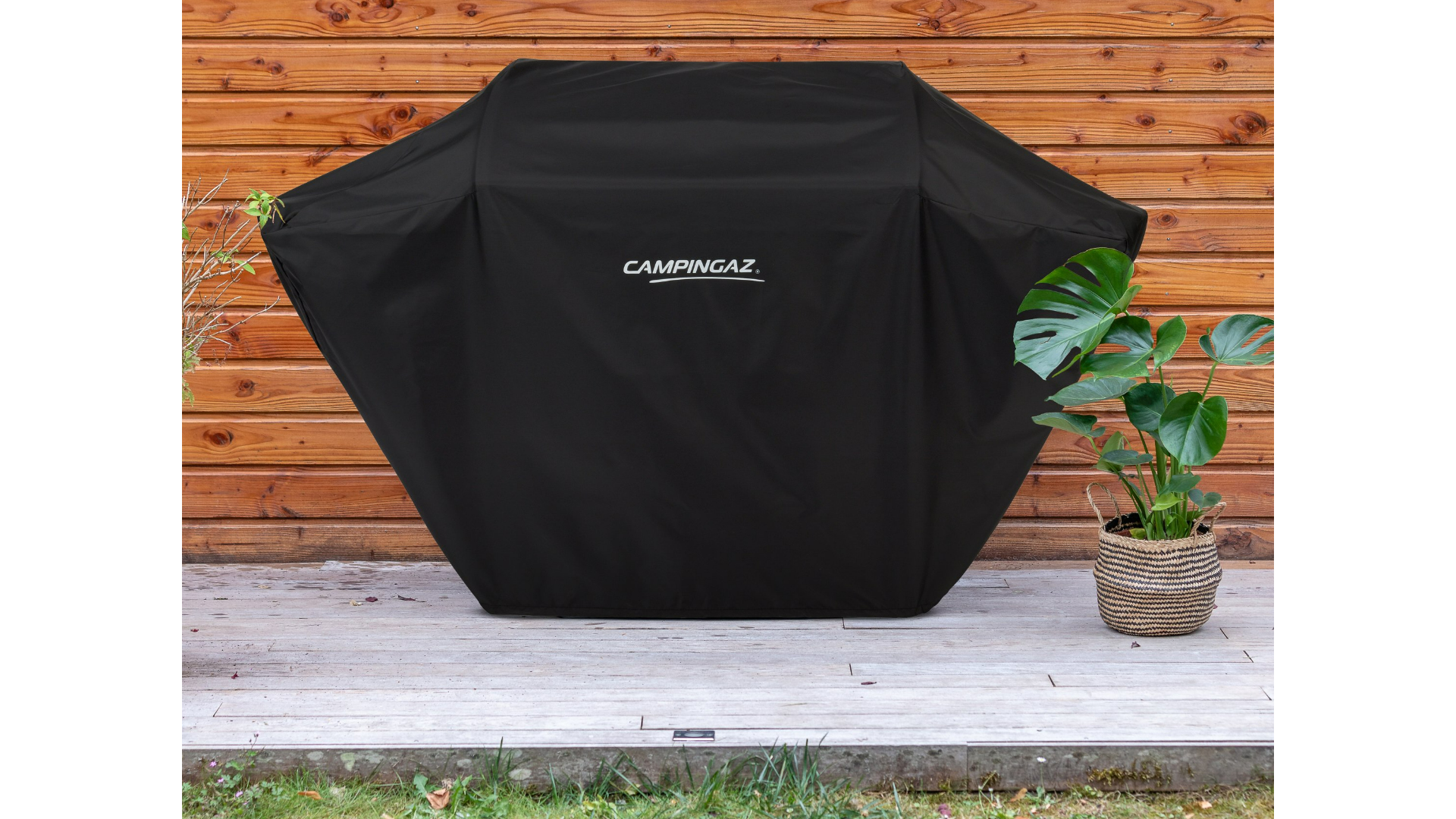 Czarna osłona grilla na drewnianym tarasie z rośliną w doniczce w koszu.
